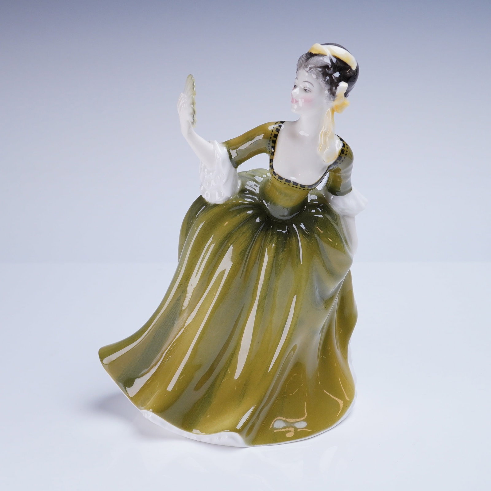 Royal Doulton Figurine Simone HN 2378: A glazed porcelain figurine titled Simone, model number HN 2378, manufactured by Royal Doulton. The figure depicts a woman in a historical-style gown, primarily finished in glossy olive green with whi