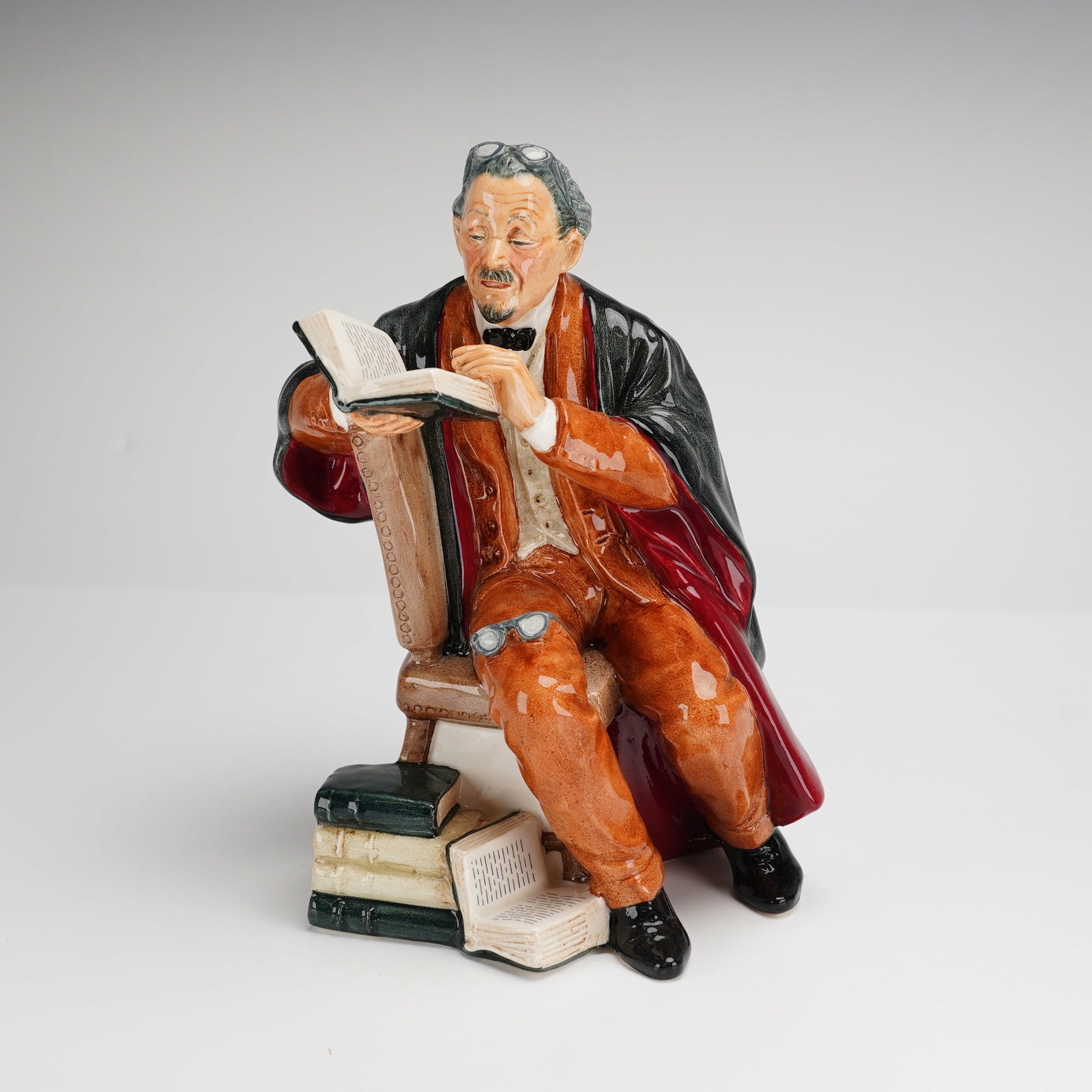 Royal Doulton Figurine The Professor HN2281: A Royal Doulton polychrome glazed porcelain figurine titled The Professor, model number HN 2281. The figure depicts a seated male in academic attire, designed by M. Nicoll. The subject is rendered wit