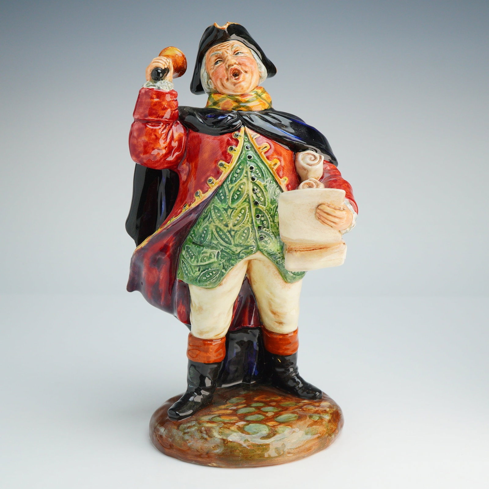 Royal Doulton Figurine Town Crier HN2119: This glazed ceramic figure was designed by L. Harradine and copyrighted in 1952. The character is depicted in 18th-century style attire, featuring a red coat over a green patterned waistcoat, white br
