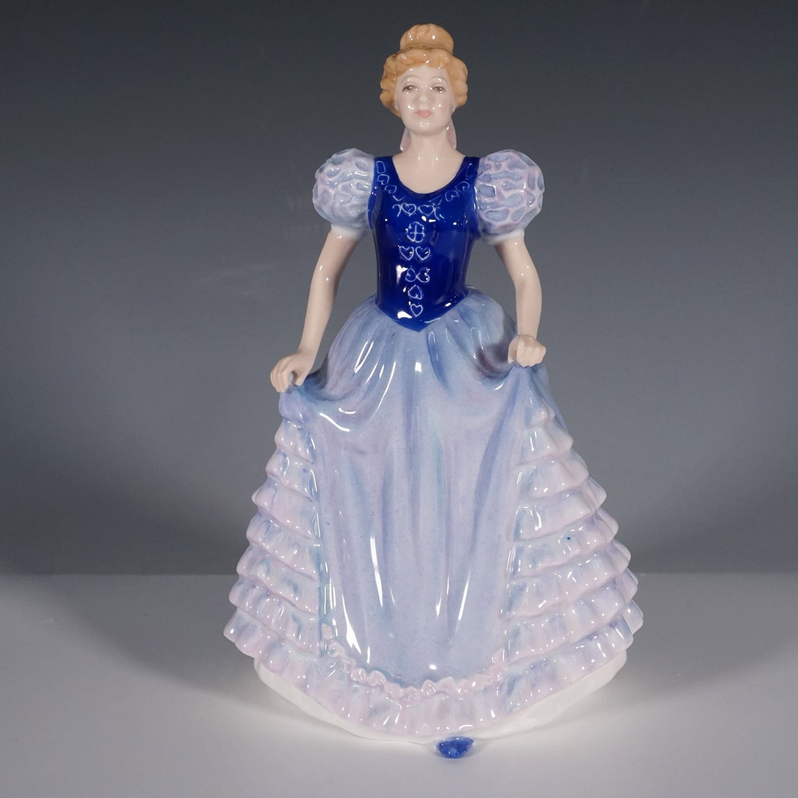 Royal Doulton Figurine, Charlotte HN3658: This Royal Doulton figurine, titled Charlotte (HN3658), features an elegant lady in a flowing blue and lavender gown, adorned with ruffled details on the skirt. The figurine stands at 8"H and is prese