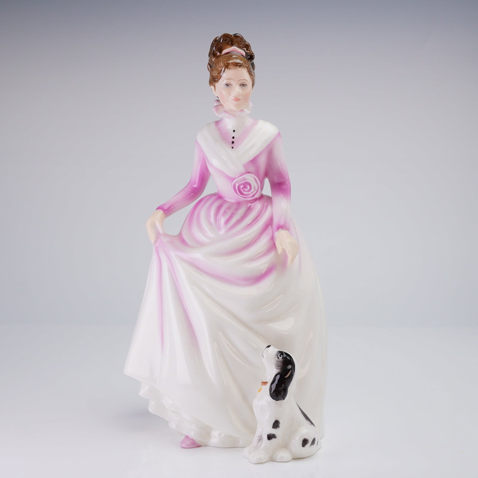 Royal Doulton Figurine, Good Companion HN3608: Modeled by Nada M. Pedley, the piece is constructed of hand made and hand decorated glazed bone china. The figure depicts a woman in an Edwardian-style gown of white with magenta accents, holding her 