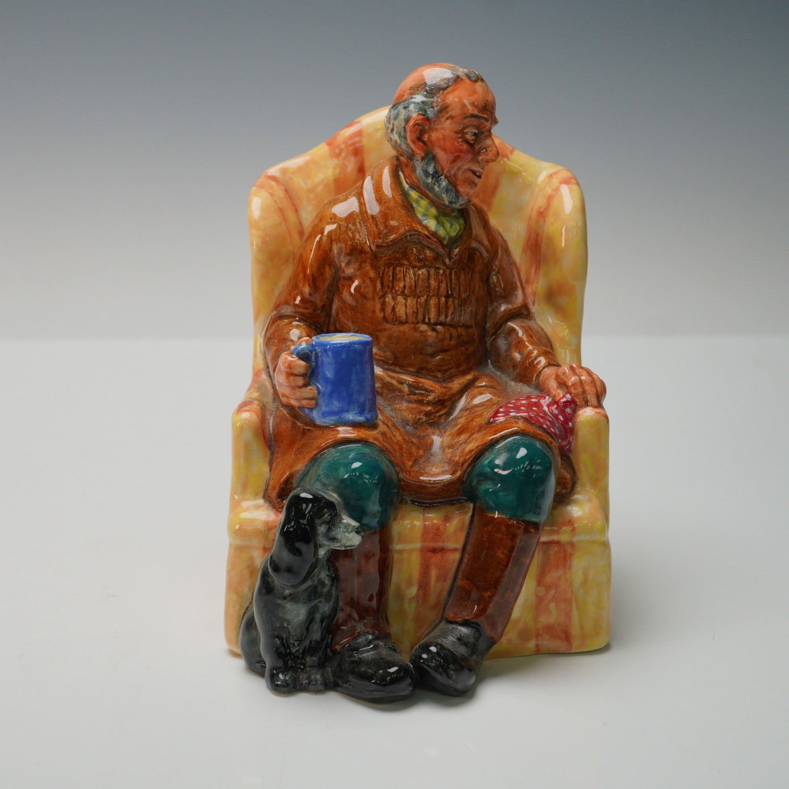 Royal Doulton Figurine, Uncle Ned HN2094: Royal Doulton figurine depicting Uncle Ned seated in an armchair with a blue mug in hand and a loyal black dog at his feet, finely modelled with detailed features and rich hand painted colours, design