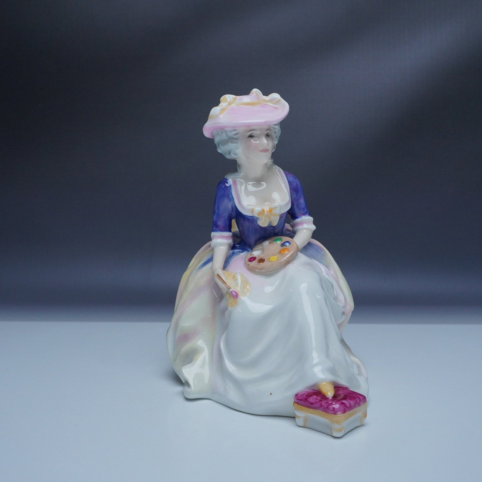 Royal Doulton Kathleen Figurine HN3100: This Royal Doulton Kathleen figurine, model HN3100, portrays a refined lady seated gracefully with a fan in hand, dressed in a flowing purple and white gown with delicate pink accents and a matching h