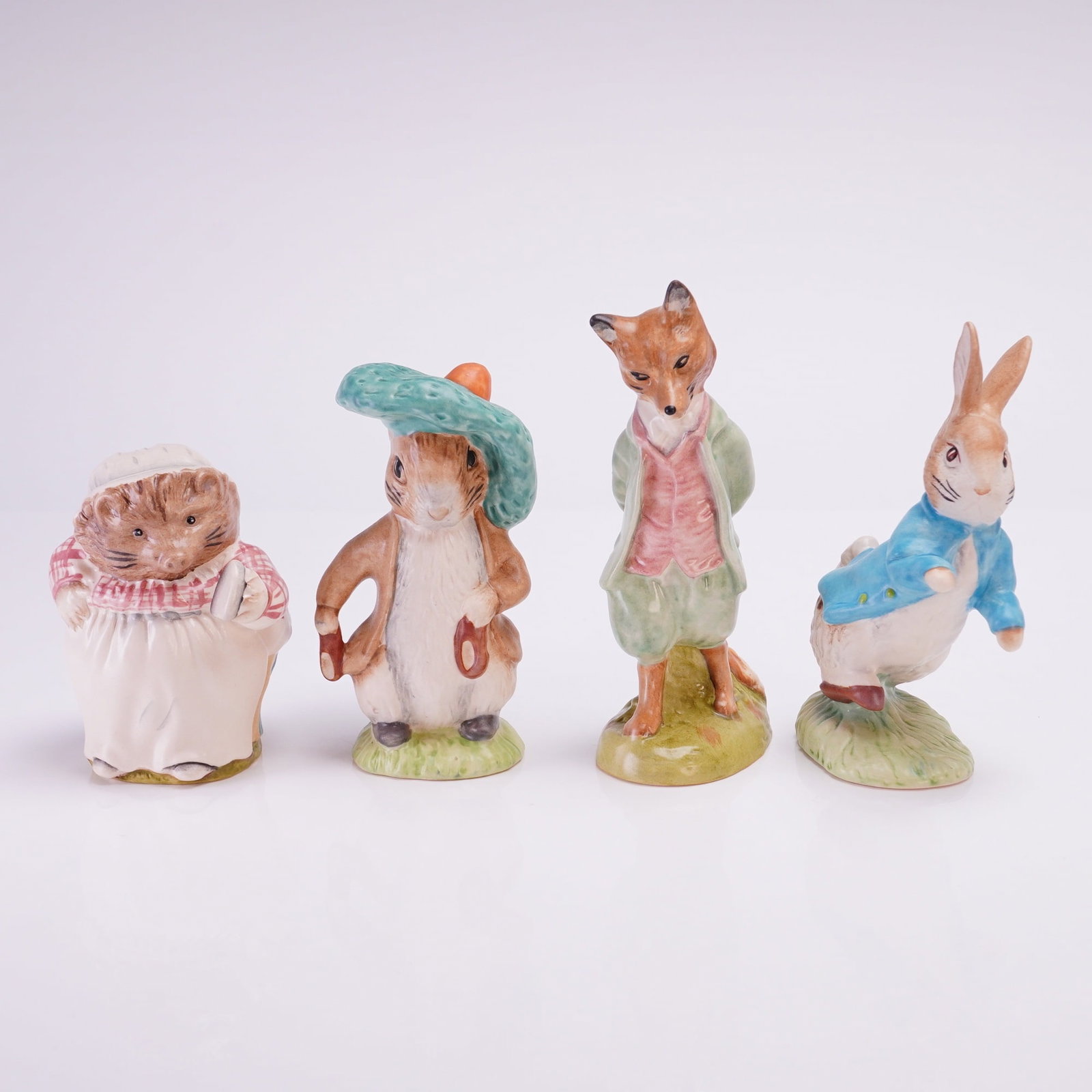 Collection of Four Beswick Beatrix Potter Figurines: A collection of four hand-painted ceramic figurines depicting anthropomorphic characters from the Beatrix Potter stories, manufactured by Beswick under license. The figures include Mrs. Tiggy-Winkle (