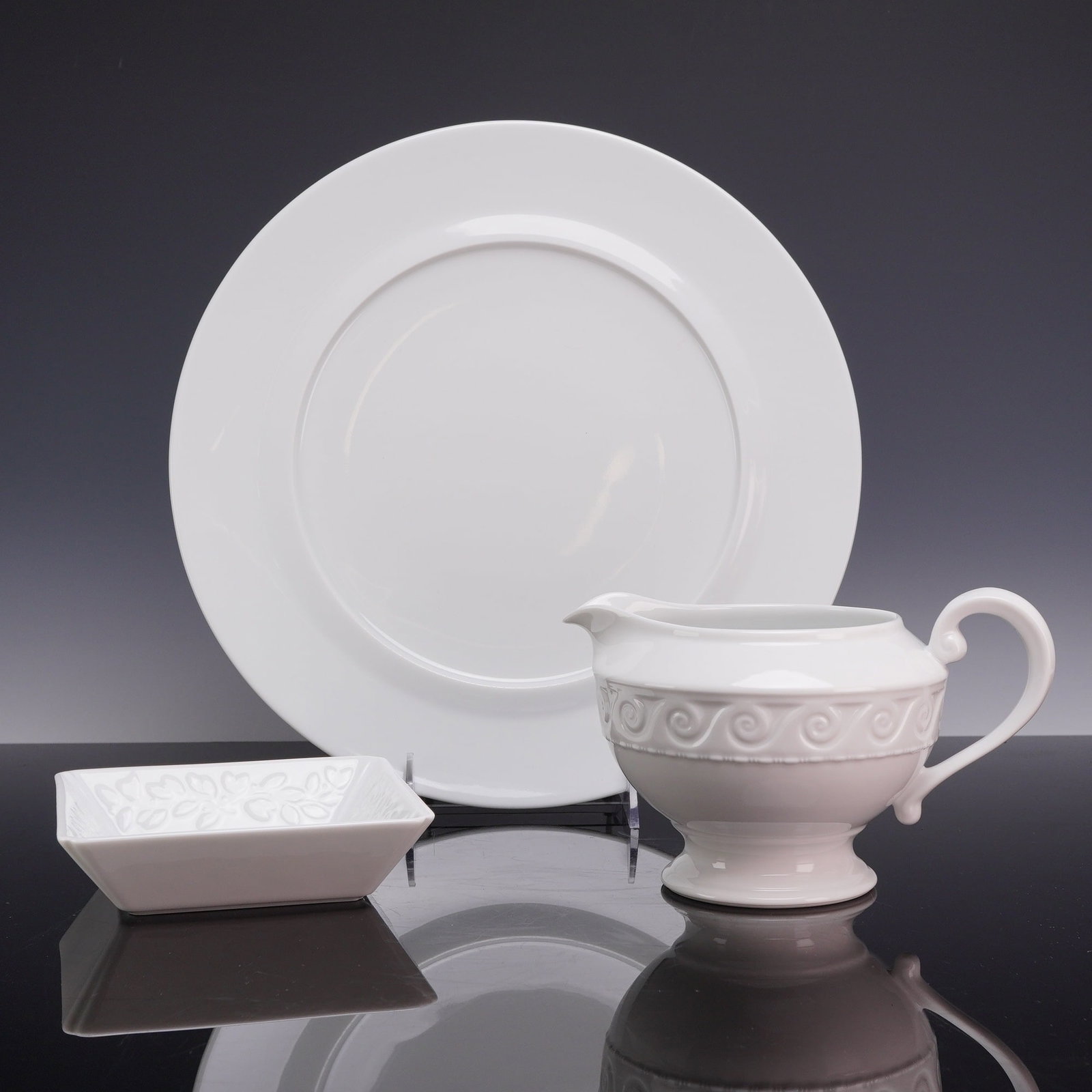 A Trio of Bernardaud Limoges White Porcelain Tableware: This three-piece collection of white glazed porcelain was manufactured by Bernardaud in Limoges, France, and two items belong to the Louvre pattern. The group includes one large service plate, one foo