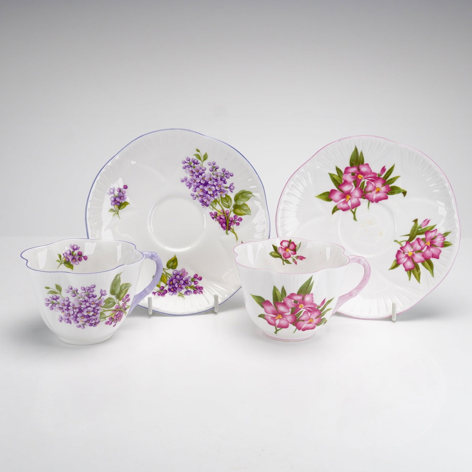 Two Sets of Shelley England Fine Bone China Cups and Saucers: This lot consists of two sets of Shelley fine bone china cups and saucers, totaling four pieces. Manufactured in England, both sets utilize the Oleander shape, which is distinguished by a wide, lobed,