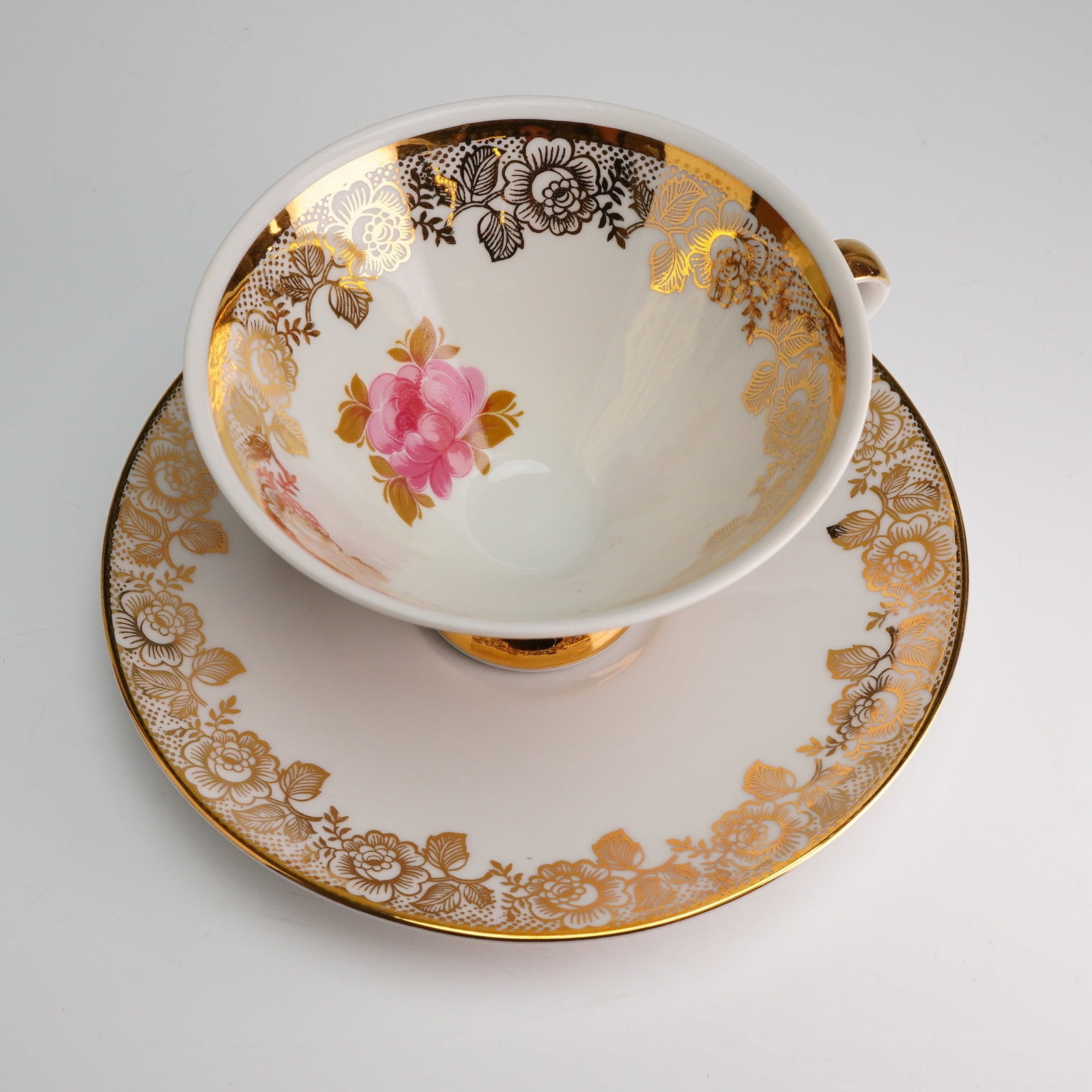 Mitterteich Bavaria Gilt Porcelain Tea Cup and Saucer: The set is constructed of white porcelain and features extensive gold transfer printing decoration. The teacup has a deep bowl shape resting upon a raised pedestal foot, with both the foot and the sim