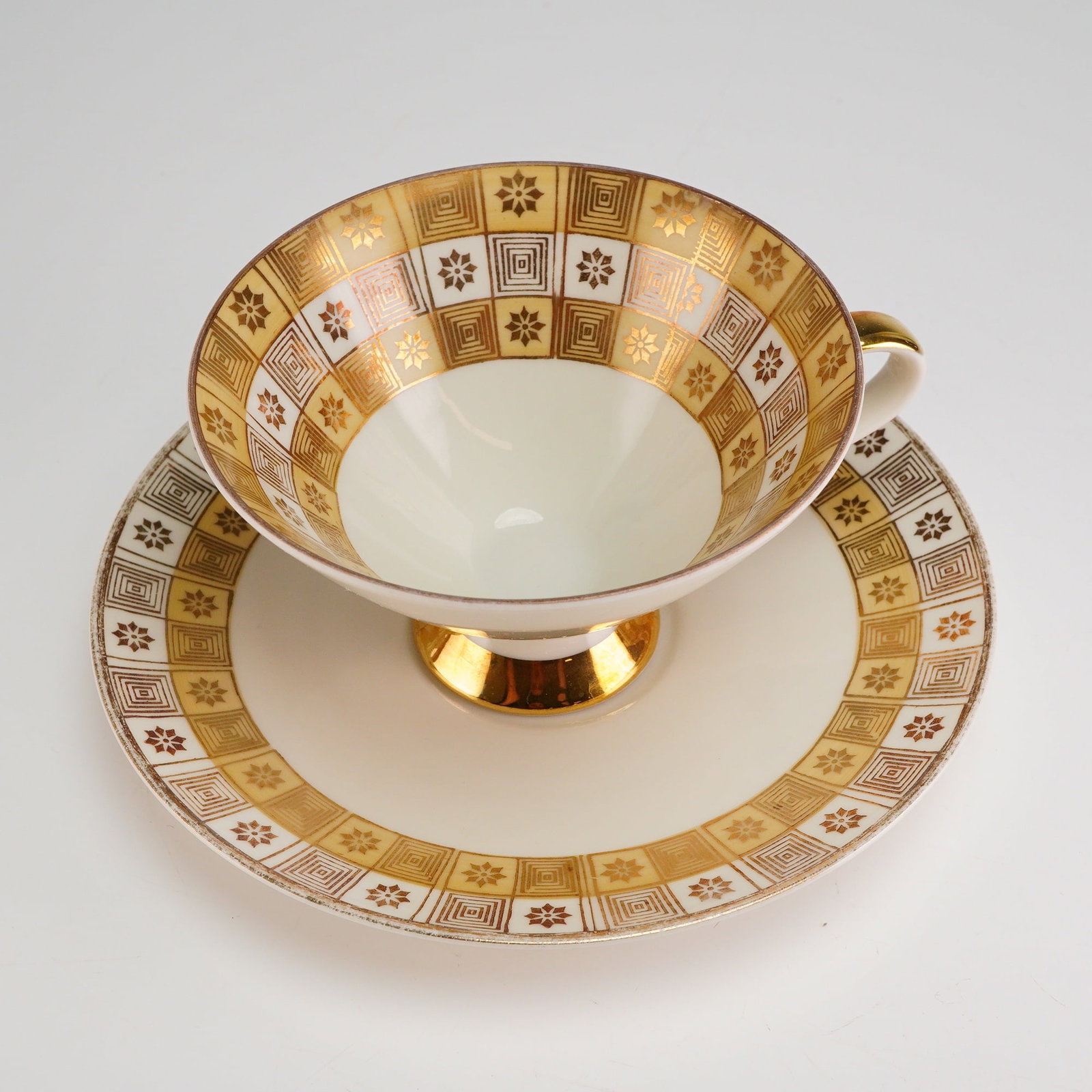 2pc Mitterteich Bavaria Porcelain Tea Set, Geometric Gilt: A 2-piece cup and saucer set executed in porcelain with heavy gold gilt accents. The set exhibits a Mid-Century modern style decoration characterized by a wide band of bold geometric patterns over a c