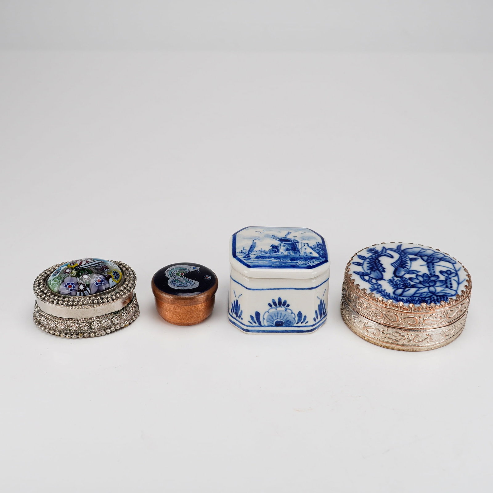 Four Decorative Treasure Pill Boxes with Blue Decorations: This collection consists of four assorted decorative boxes of various materials and styles. The first is an oval-shaped silver-tone metal box featuring filigree and granulated beadwork details. Its