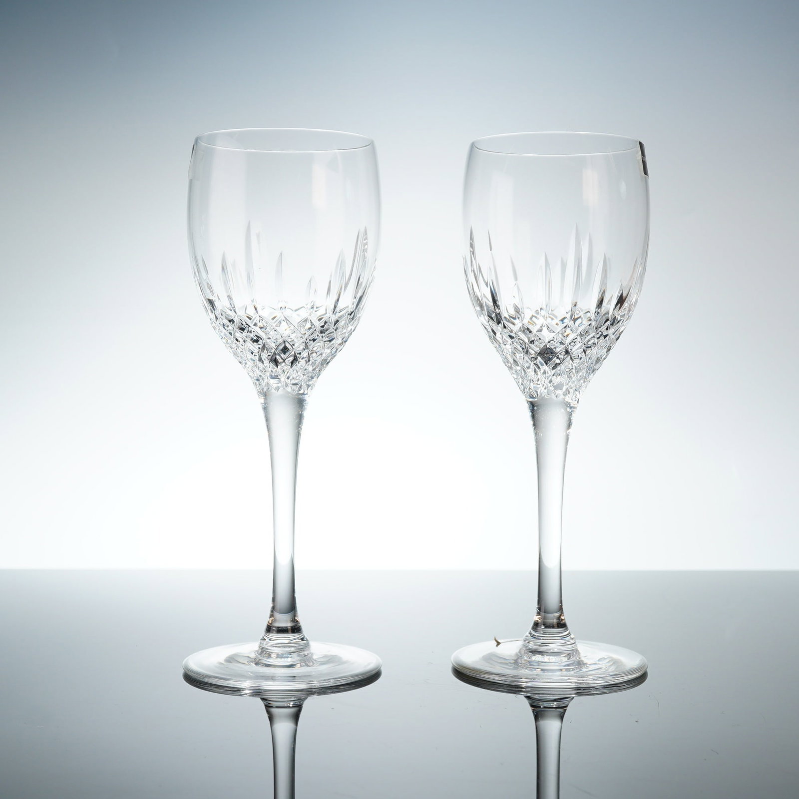 Pair of Dartington Crystal Wine Glasses: Each glass features a clear crystal bowl decorated with a lower register of diamond-cut cross-hatching beneath a band of vertical wedge cuts. The bowls are supported by elongated, tapered plain stems 