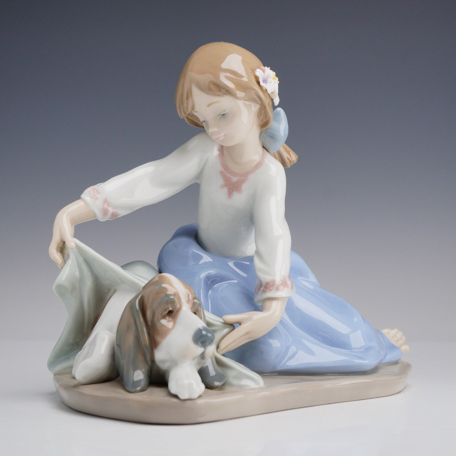 Lladro Porcelain Figurine Dog's Best Friend 01005688: Designed by sculptor Antonio Ramos and first issued in 1990, this retired piece features a sentimental scene of a young girl tending to a sleeping basset hound. The girl is depicted in a seated pose