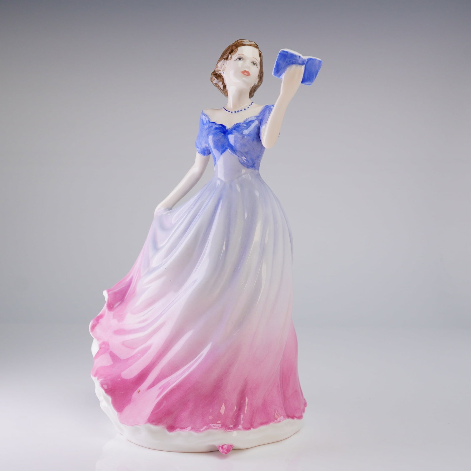 Royal Doulton Figurine Sweet Poetry HN4113: A glazed porcelain figurine by Royal Doulton, titled 'Sweet Poetry.' The figure depicts a young woman in a formal, flowing gown featuring a dramatic color gradient from blue at the bodice, transitioni