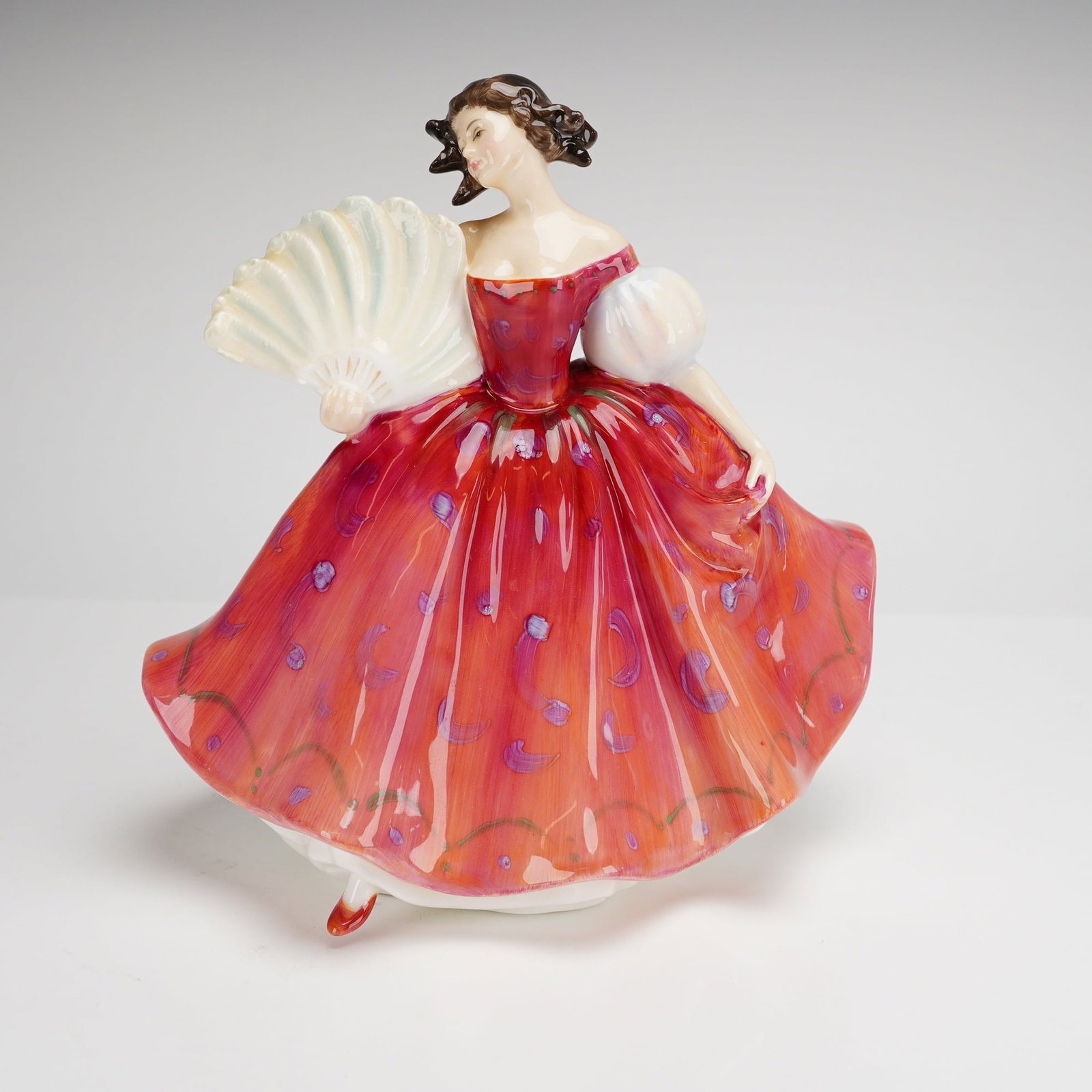 Royal Doulton Bone China Figurine First Waltz HN2862: A Royal Doulton bone china figurine titled First Waltz, model number HN2862. The piece depicts a female figure in a full-skirted gown decorated in shades of red and orange with purple crescent-shaped 