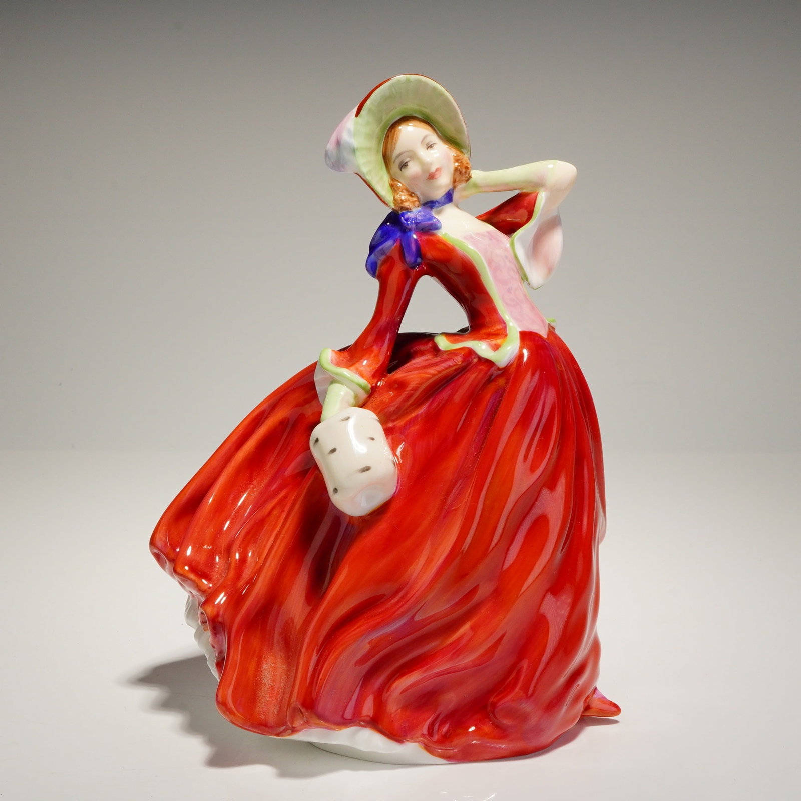 Royal Doulton Figurine Autumn Breezes HN1934: A Royal Doulton bone china figurine titled "Autumn Breezes," model number HN 1934. The figure depicts a young woman in period attire, modeled in a dynamic pose suggesting movement, with her voluminous
