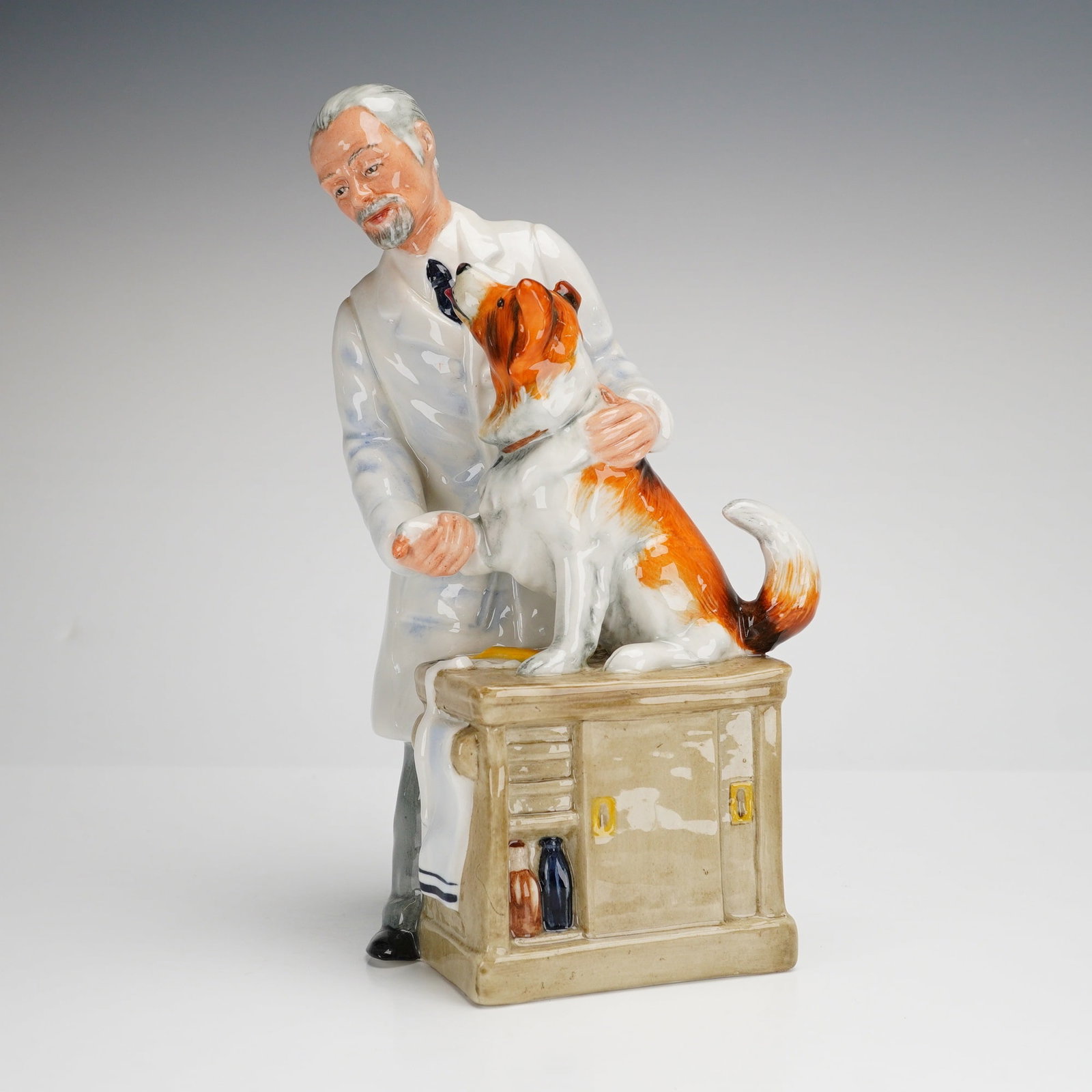 Royal Doulton Figurine Thanks Doc! HN2731: A Royal Doulton glazed porcelain figurine titled Thanks Doc! model HN 2731. The figure depicts a grey-haired veterinarian in a white lab coat tending to a tri-color collie dog. The dog is positioned o