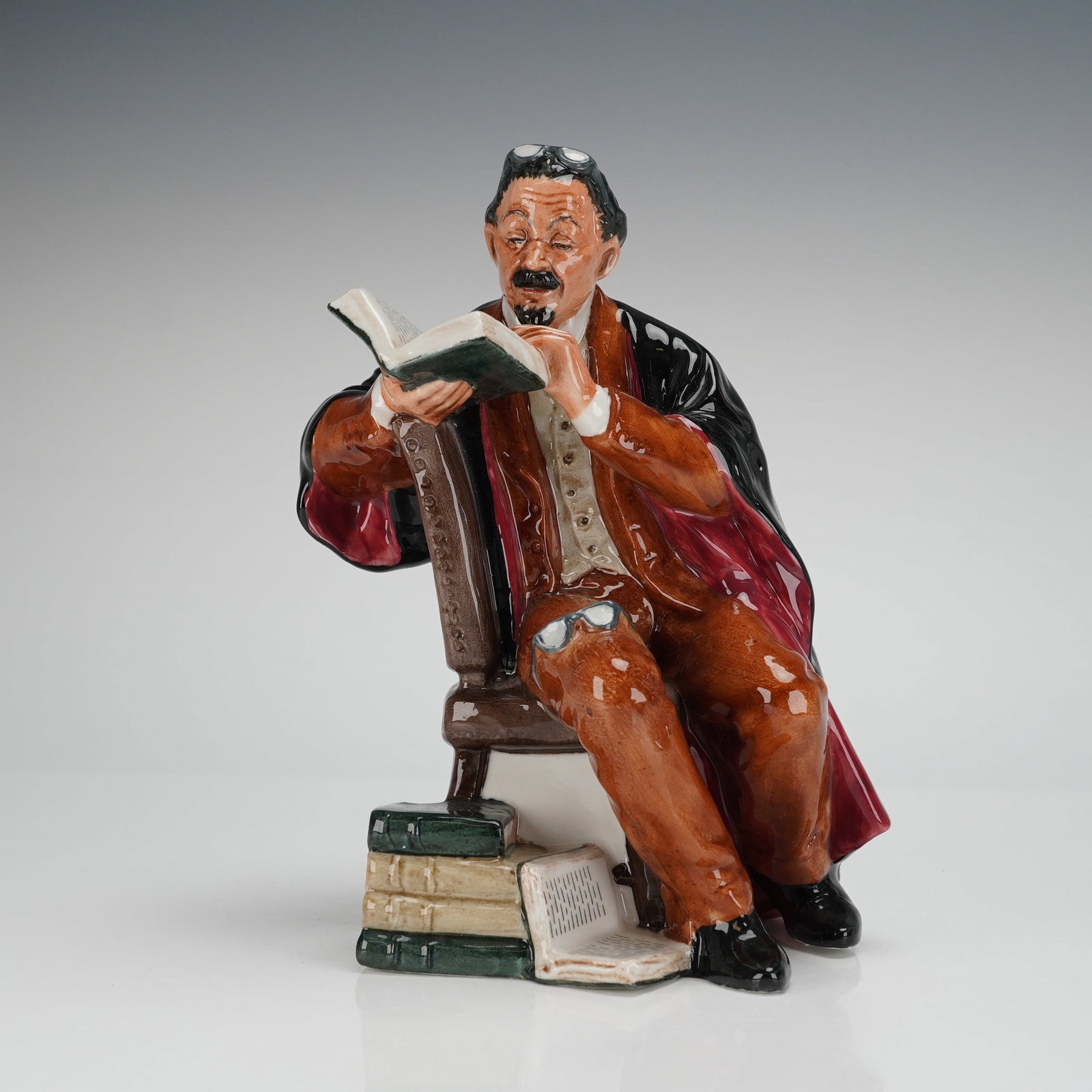 Royal Doulton Figurine The Professor HN2281: A vintage Royal Doulton Figurine depicting a seated male academic figure. The figurine is executed in high gloss glazed ceramic. The figure is dressed in a rust-brown suit and waistcoat, covered by a 