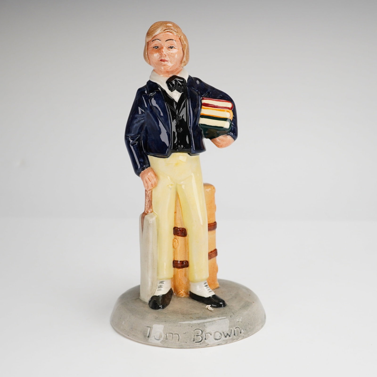 Royal Doulton Figurine Tom Brown HN2941: This Royal Doulton figurine, titled Tom Brown HN2941, is a hand-painted porcelain figure from the Children's Literature series. Designed by William Harper and issued in 1982, the piece depicts a schoo