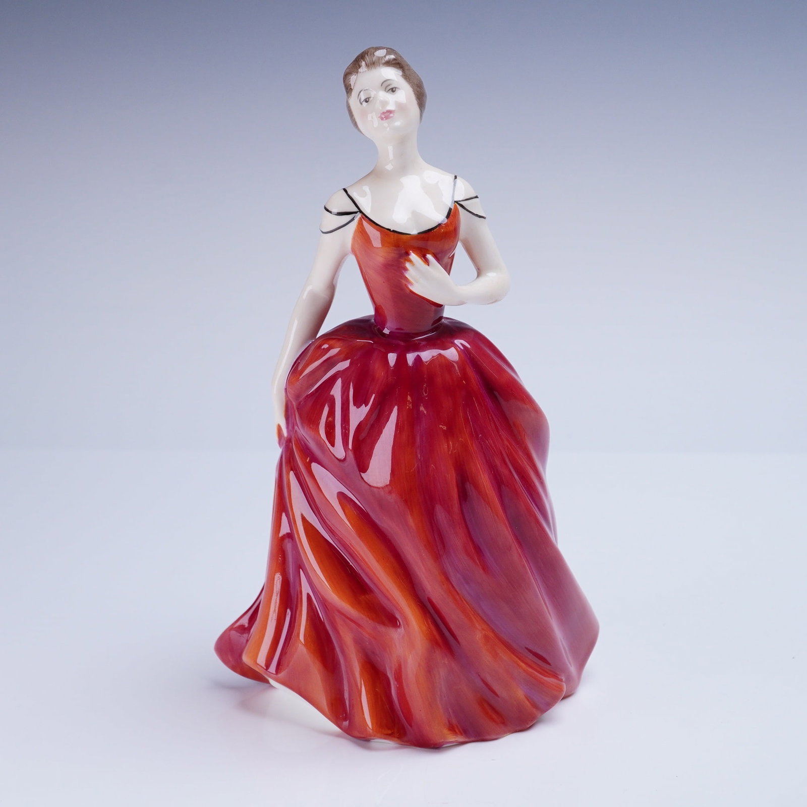 Royal Doulton Figurine, Innocence HN 2842: A figurative ceramic Royal Doulton figurine titled "Innocence." The piece is executed in glazed and painted bone china, depicting a woman in a voluminous, flowing crimson/red evening gown with painted