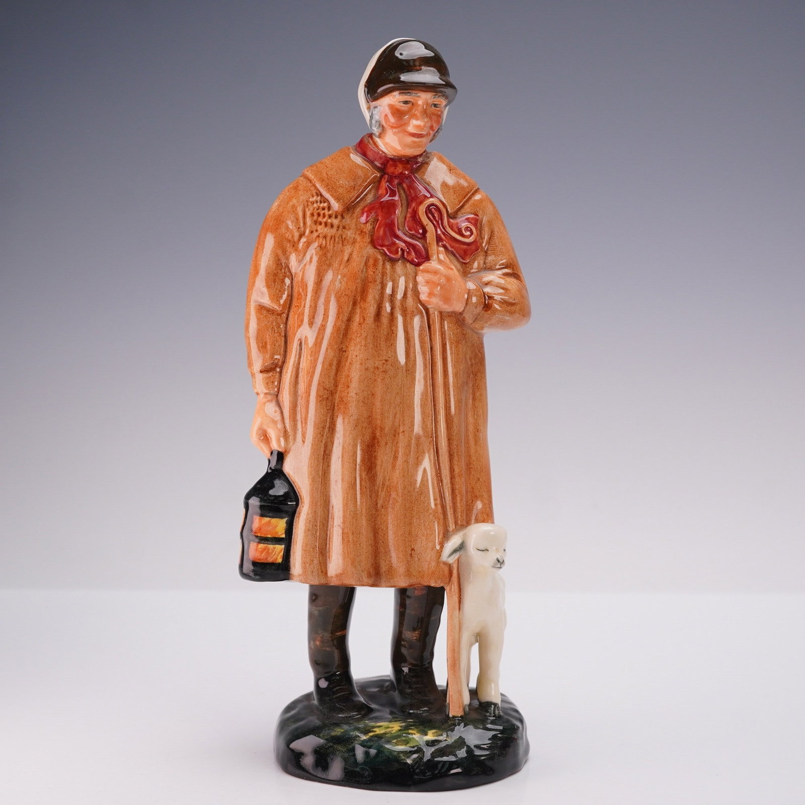 Royal Doulton Figurine, Shepherd HN1975: Crafted in hand-painted porcelain, the piece depicts a shepherd dressed in a long brown overcoat with a red scarf and black hat, holding a staff and a lantern. At his side stands a small lamb, adding 