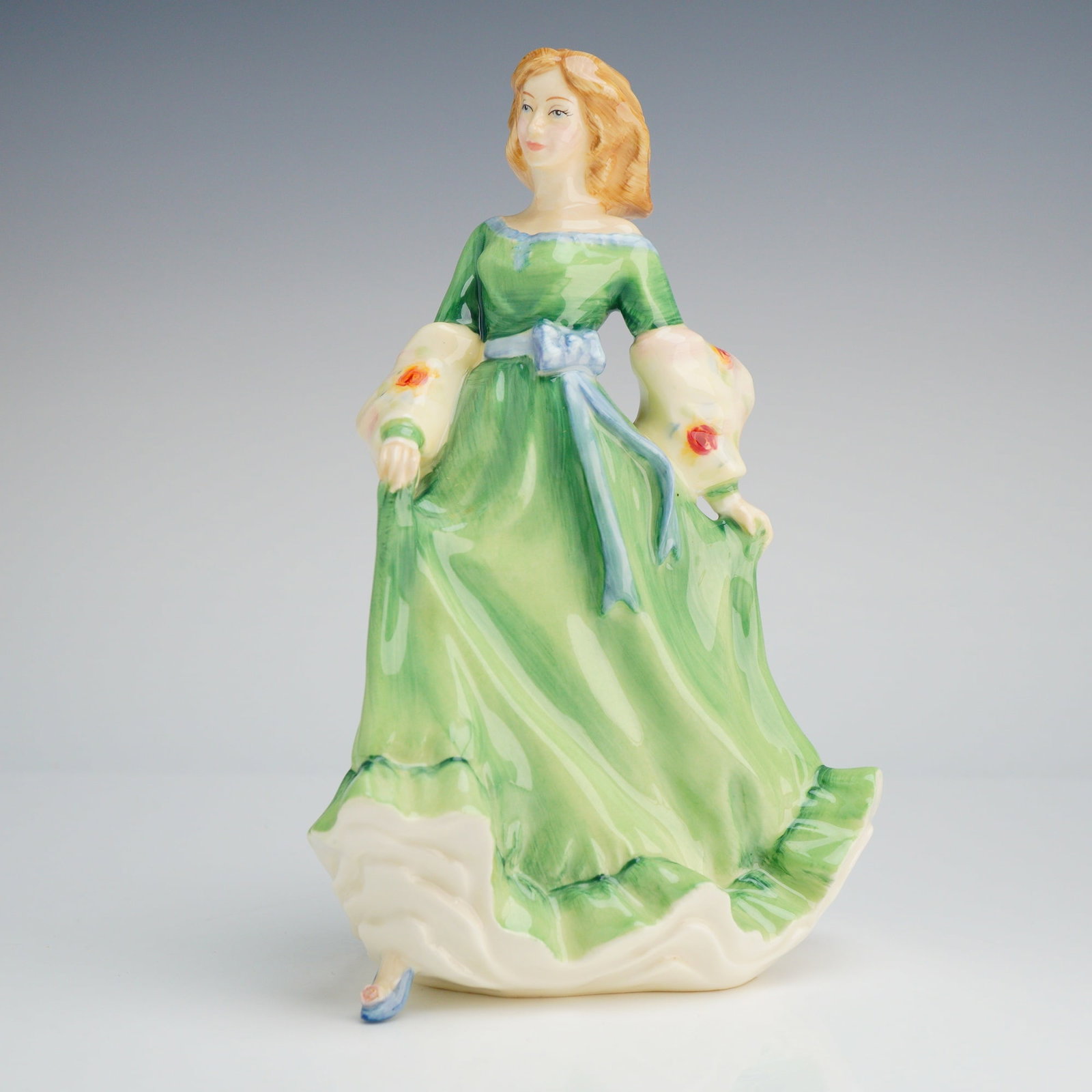 Royal Doulton Figurine, Spring Serenade HN3956: The hand-decorated figure depicts a woman in a flowing, high-waisted, vibrant lime-green dress accented with a light blue sash. She wears elaborate floral-patterned sleeves or a shawl. The base is mar