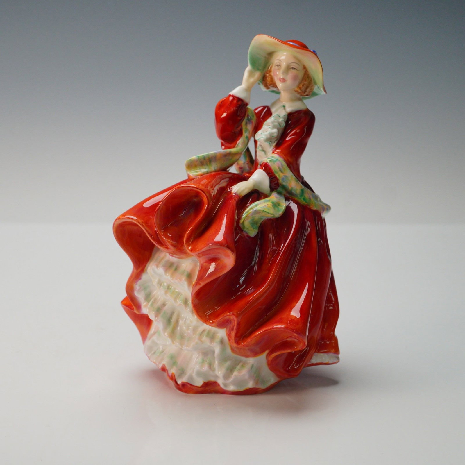 Royal Doulton Figurine, Top O' The Hill HN3499: A Royal Doulton bone china figurine depicting the classic Top O' The Hill design, model HN3499, featuring a young lady in a flowing red dress with white petticoats, accented with green trim, holding h