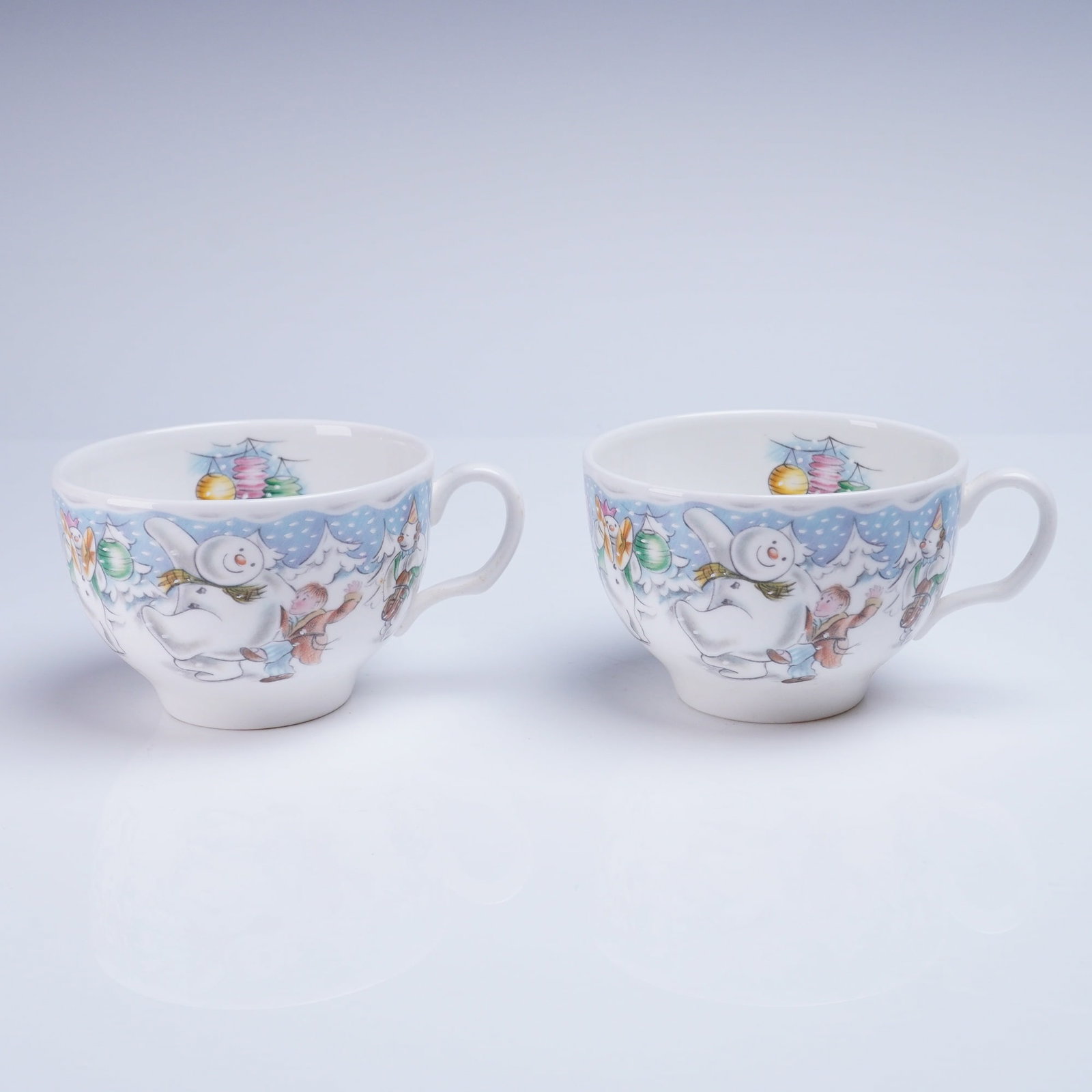 2pc Royal Doulton Snowman Partytime Teacups: A group of contemporary teacups manufactured by Royal Doulton, in the "Snowman Partytime" pattern, which is part of The Snowman Gift Collection. The cups are constructed of white Bone China. Each cup 