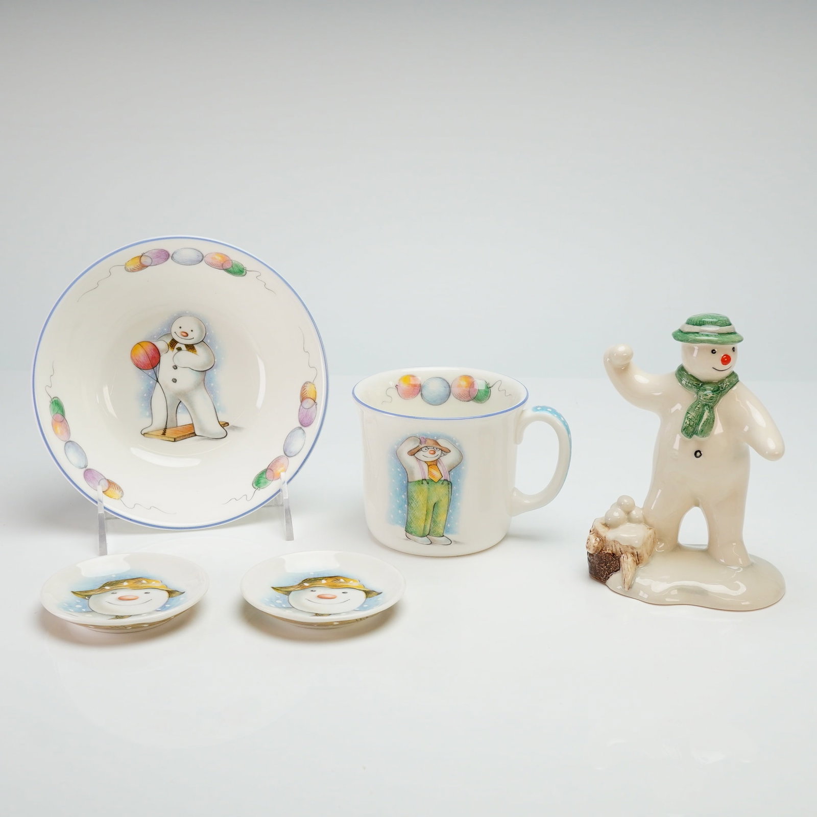 5pc Royal Doulton Snowman Gift Collection Figurine, Cup and Plate: Collection featuring bone china and ceramic items with illustrations from the holiday story. The set includes a figurine titled The Snowman Snowballing (DS 22), a mug, a bowl, and two small dishes. Th