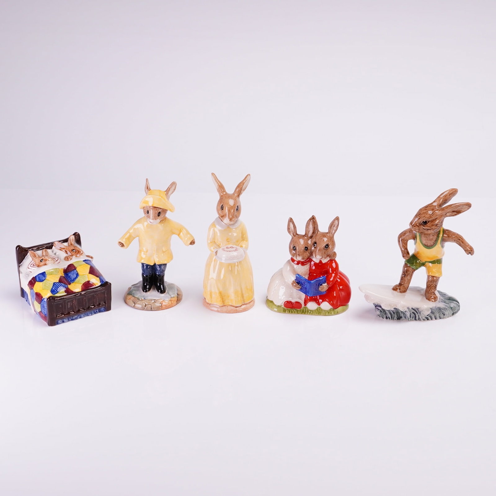 Collection of Five Royal Doulton Bunnykins Figurines: A collection of five collectible ceramic figurines manufactured by Royal Doulton, part of the popular Bunnykins series. The figures are rendered in glazed porcelain or bone china with bright polychrom