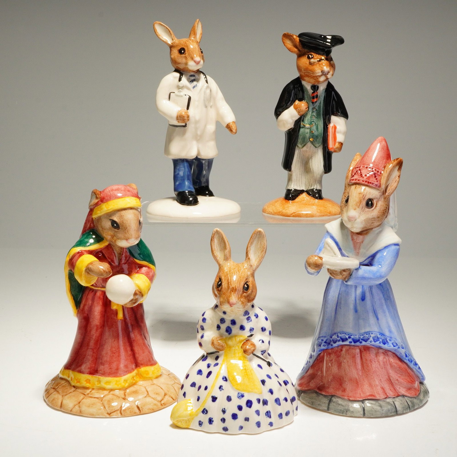 5pc Royal Doulton Bunnykins Fortune Teller School Master Susan Doctor: A collection of five Royal Doulton Bunnykins porcelain figurines. Each figure is crafted from hand-painted ceramic with a high-gloss glaze finish. The group includes Fortune Teller DB218 depicted in a