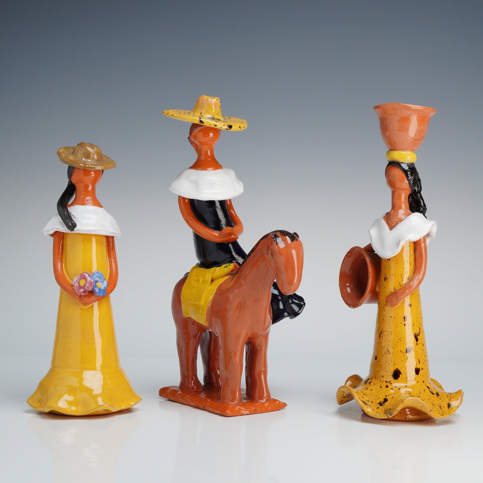 3pc Faceless Folk Art Terracotta Female Figurines: Terracotta figurines depicting stylized figures in traditional attire, including a woman holding flowers, a man on horseback, and a woman carrying vessels. The pieces are crafted from terracotta and f