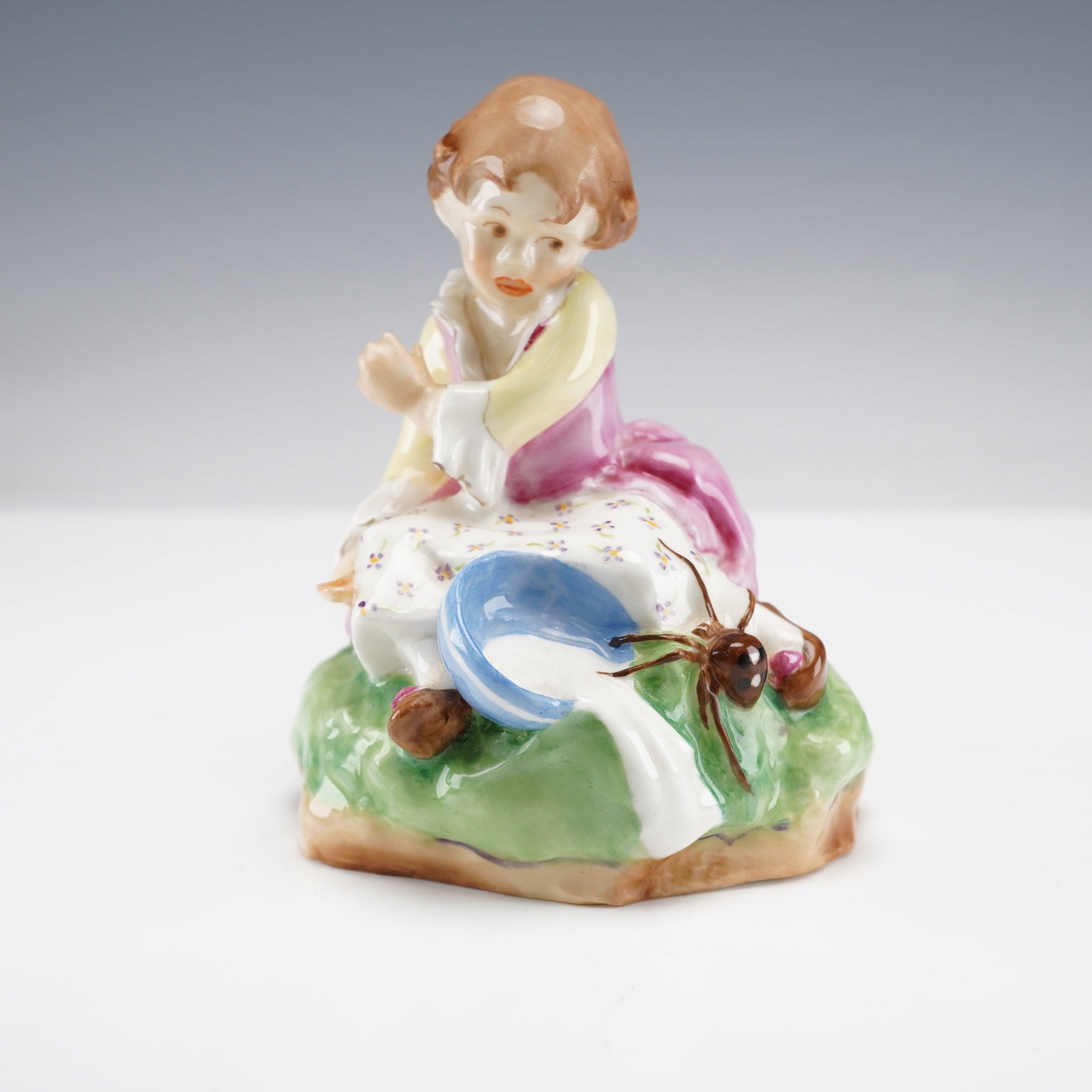Royal Worcester Figurine, Little Miss Muffet 3301: A nursery rhyme figure modeled as a character seated upon a grassy mound, dressed in a rose-pink pinafore over a floral-patterned white skirt, captured in a moment of surprise as a spider approaches h