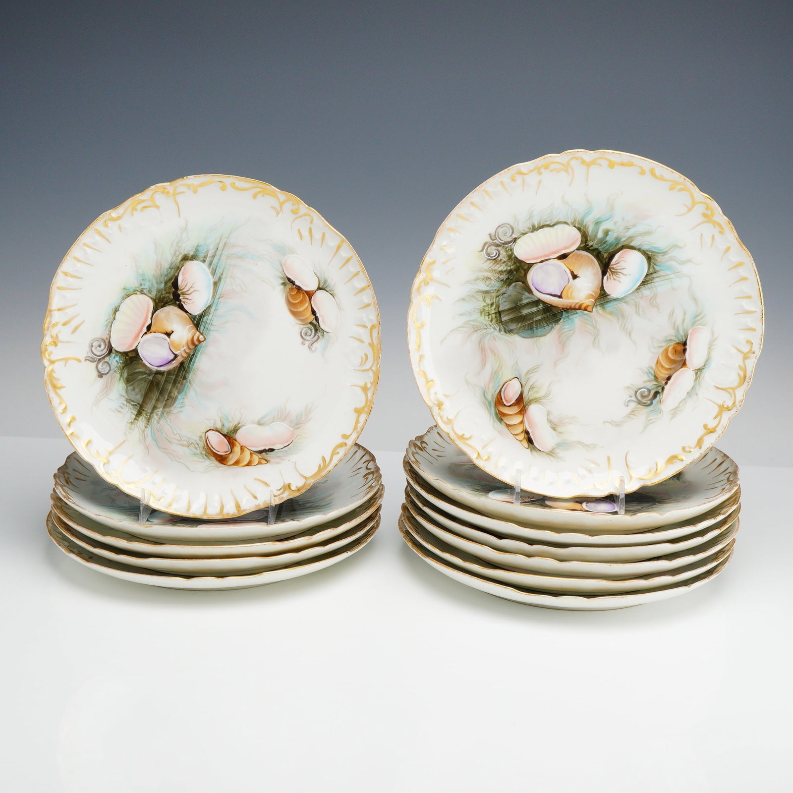 Set of 12 Jean Pouyat Limoges Hand-Painted Porcelain Dessert Plates, Shell Motif: This is a set of 12 fine porcelain dessert or cabinet plates produced by the Jean Pouyat factory in Limoges, France. Each circular plate features a scalloped and relief-molded rim decorated with scrol