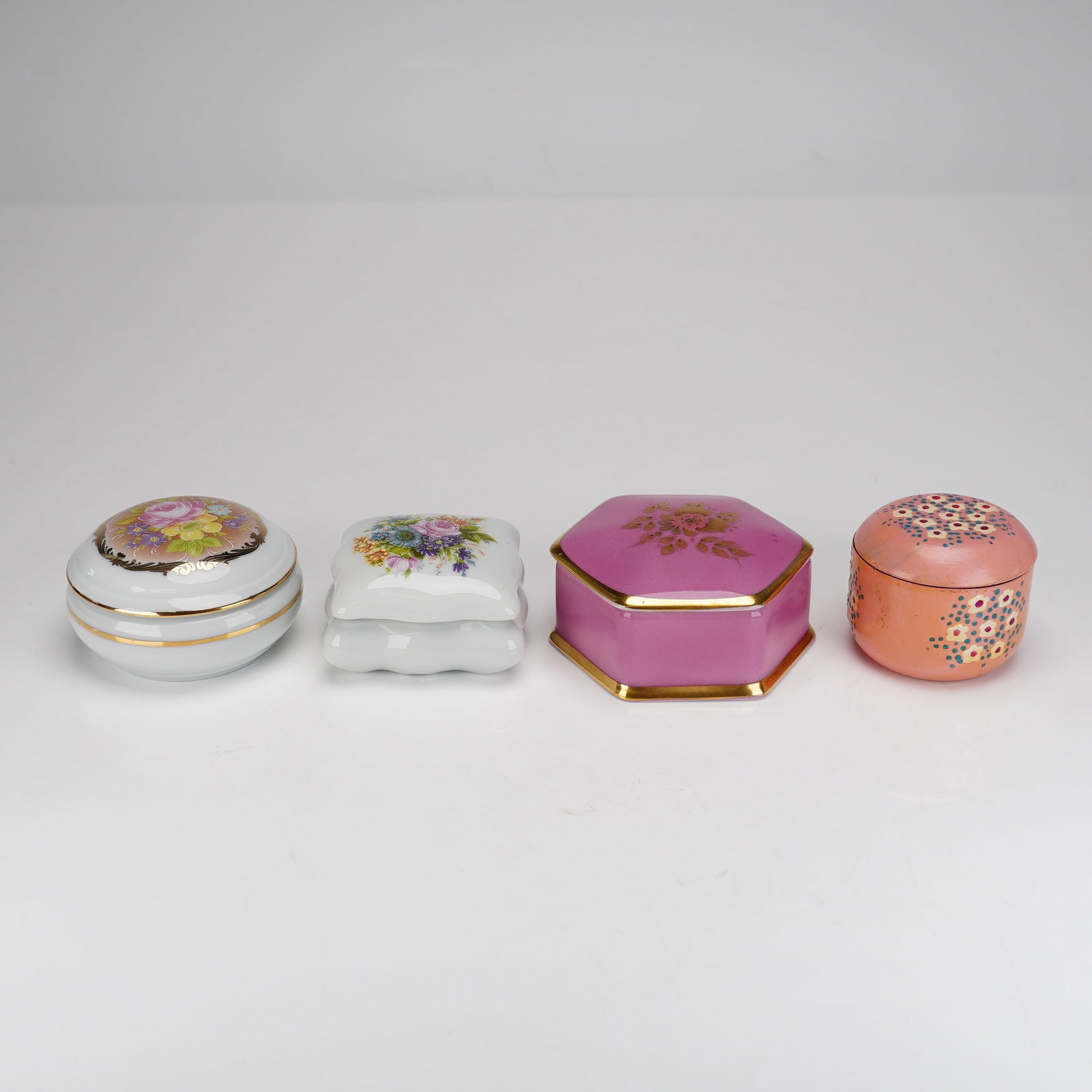 Four Decorative Floral Treasure Boxes, Limoges and Gloria Bavaria Porcelain: This lot comprises four decorative lidded treasure boxes featuring floral motifs and varying forms. Two examples are crafted from white porcelain and originate from Limoges, France. The first is a cir