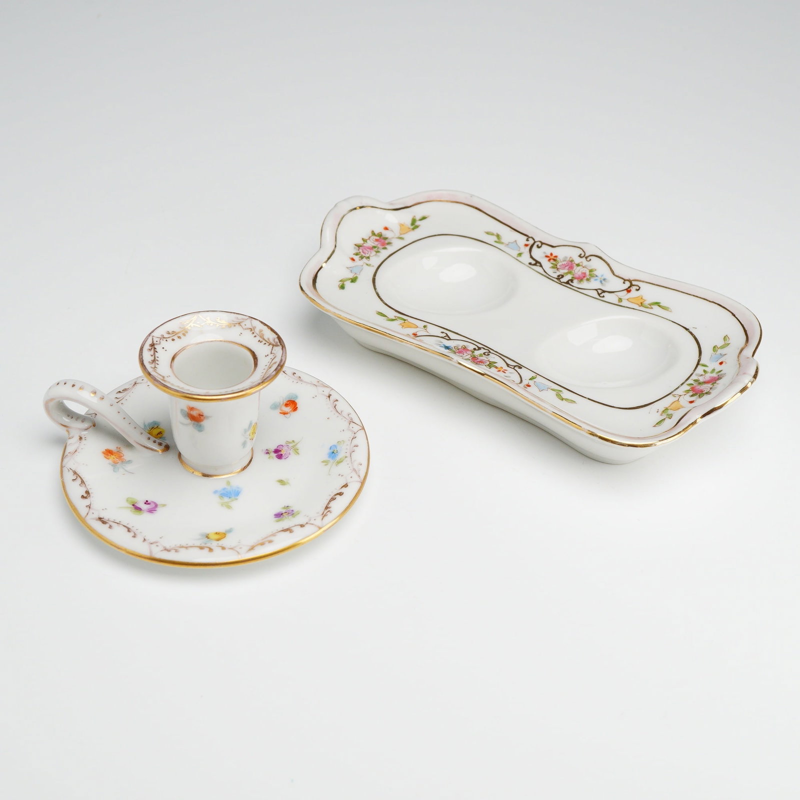 Two Richard Klemm Dresden Porcelain Chamberstick and a Nippon Egg Holder: This lot features a two-piece porcelain grouping consisting of a hand-painted chamberstick and a rectangular tray. The chamberstick, of German origin, was produced by the Richard Klemm studio in Dresd