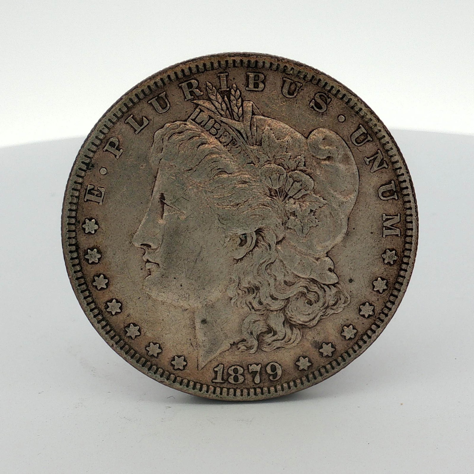 1879 US One Dollar Morgan Silver Dollar, Circulated: This US 1879 Morgan silver dollar is a Philadelphia-minted specimen composed of 90 percent silver and 10 percent copper. The coin features the Morgan dollar design. The obverse includes the date 1879 