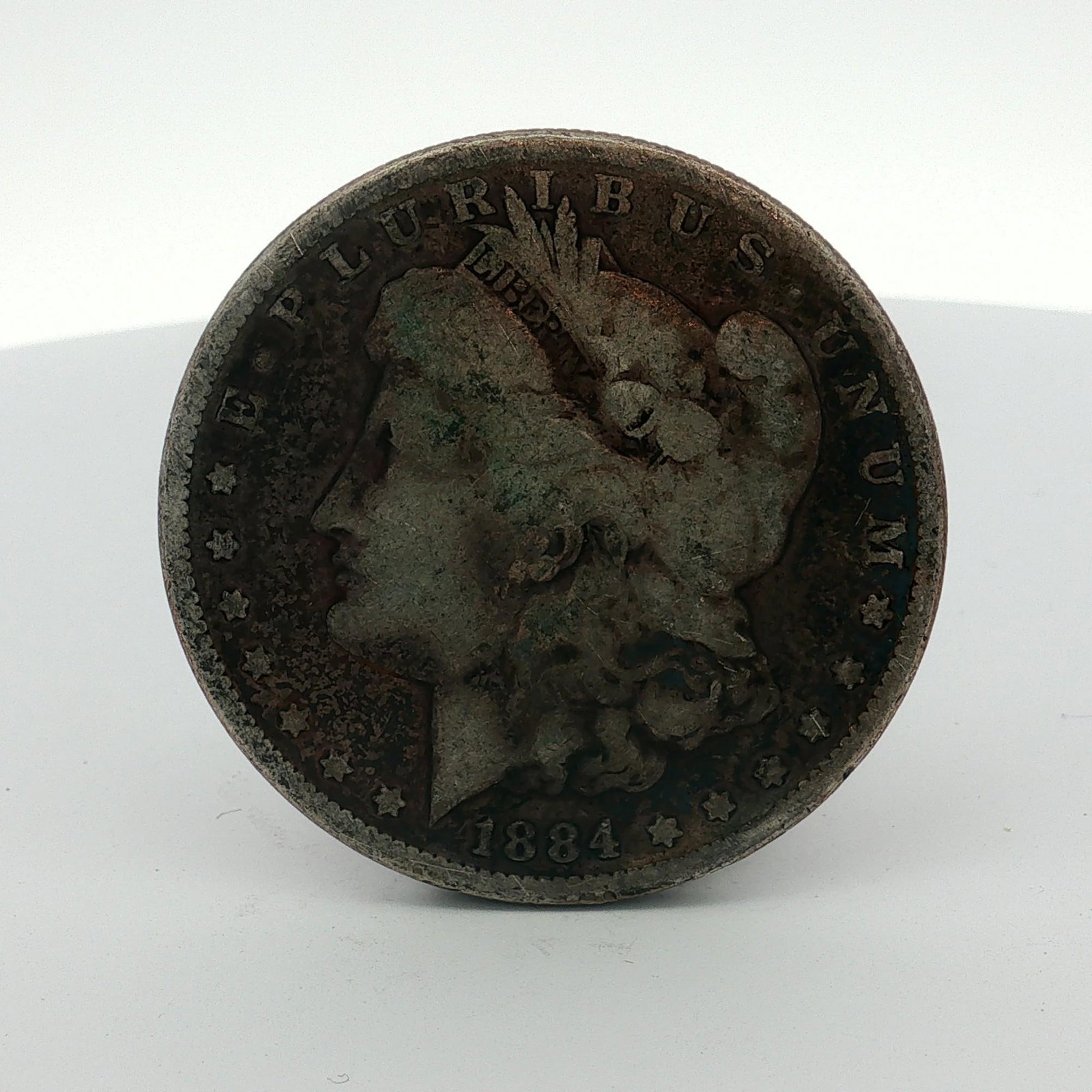 1884 US One Dollar Morgan Silver Dollar, Circulated: This US Morgan dollar is dated 1884 and was struck at the Philadelphia Mint. The coin is composed of 90% silver and 10% copper with a reeded edge. The obverse features the Liberty head design, and the