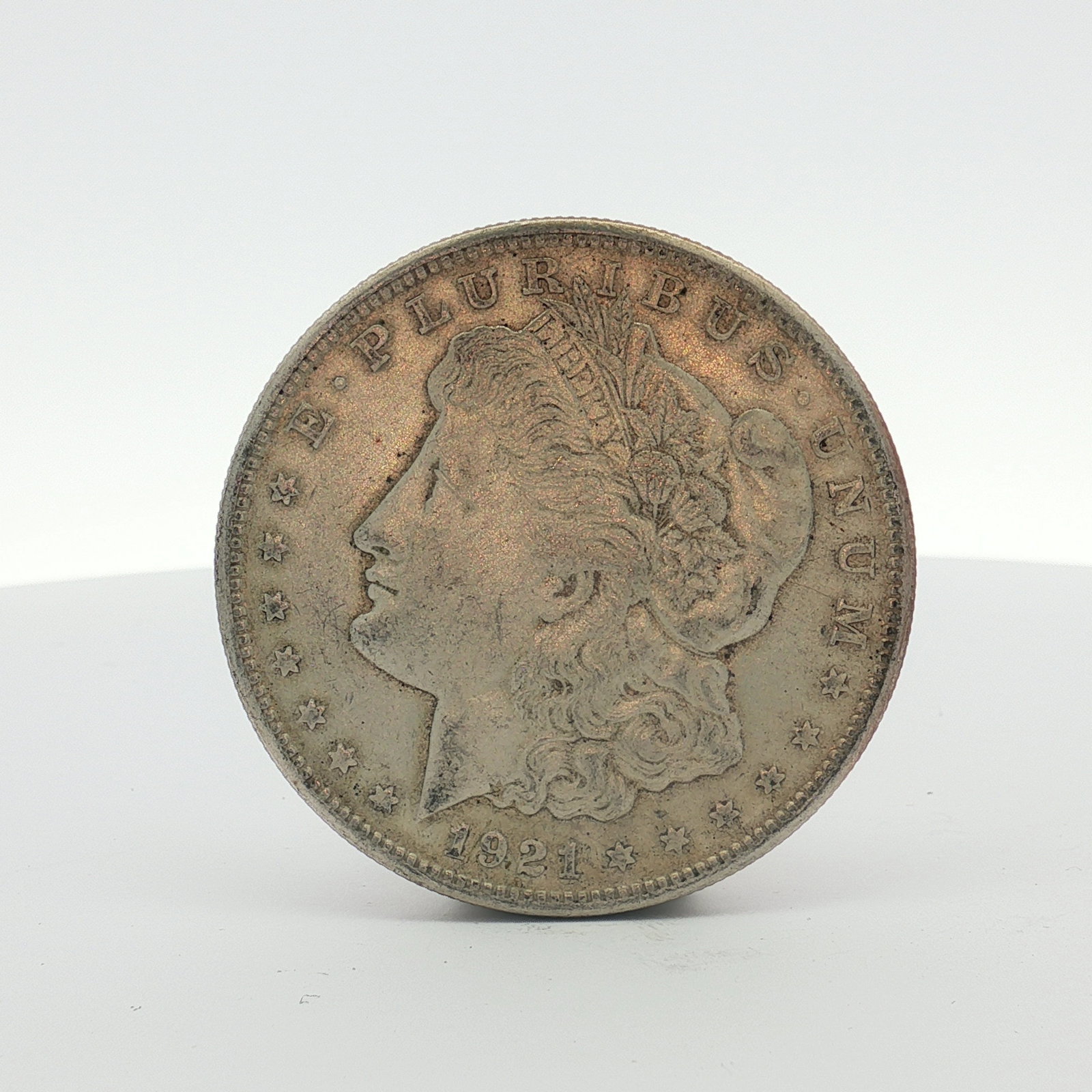 1921 US Morgan Silver Dollar Coin Circulated: This 1921 US Morgan silver dollar was struck at the Philadelphia Mint. The coin is composed of 90% silver and features a reeded edge. The obverse features the Morgan dollar Liberty head design, and th