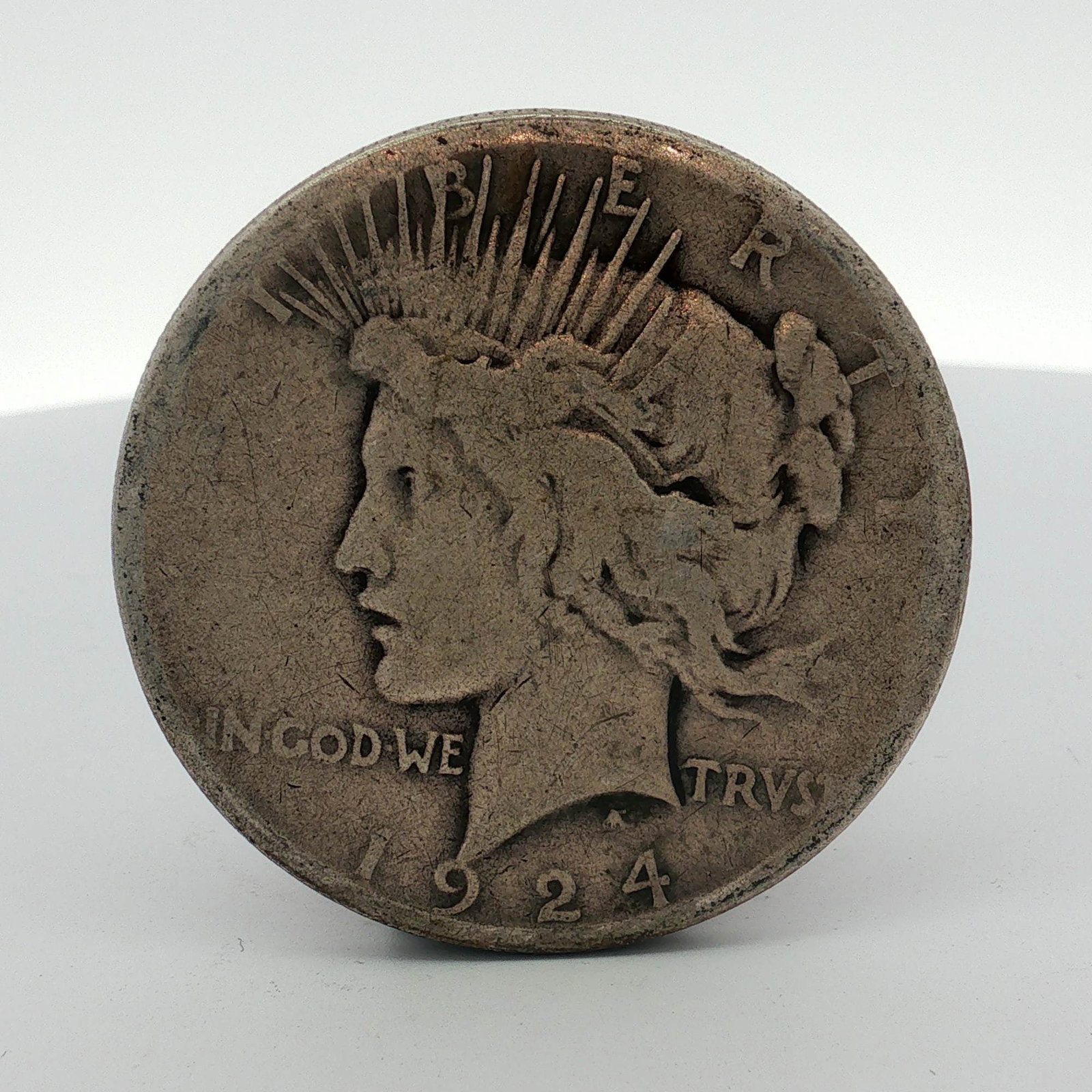 1924-S US One Dollar Peace Silver Dollar Coin, Circulated: This 1924-S US Peace silver dollar is composed of 90% silver and 10% copper. The obverse features the standard Peace dollar design by Anthony de Francisci, depicting a profile of Liberty with a radiat
