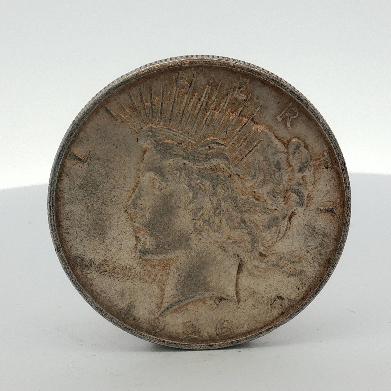 1926-D US One Dollar Peace Silver Dollar, Circulated: This US Peace silver dollar was struck at the Denver Mint in 1926. The coin features the Liberty Head design on the obverse and the Peace Eagle design on the reverse. The D mint mark is located on the