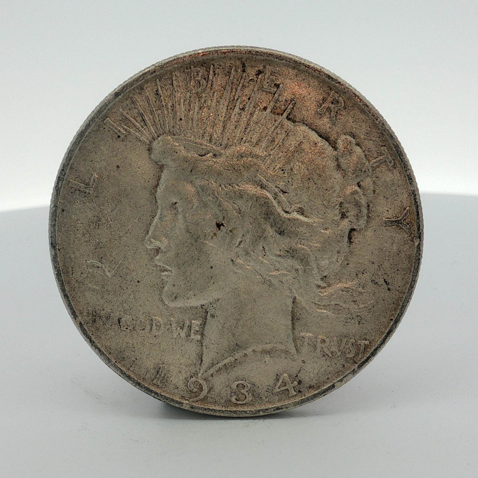 1934-D US One Dollar Peace Silver Dollar, Circulated: This US Peace dollar was struck at the Denver Mint in 1934. The coin features the Peace dollar obverse and reverse designs. The D mint mark is located on the reverse above the eagle tail feathers. The