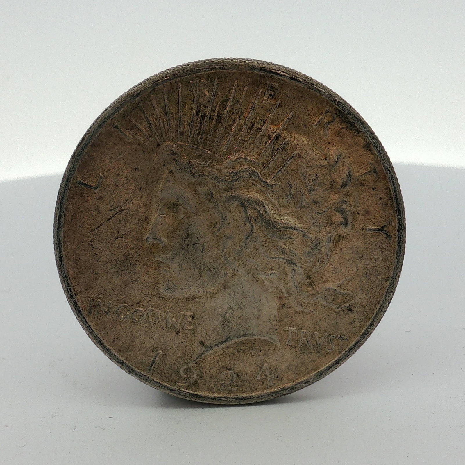 1924 US Peace Silver Dollar: This US Peace Silver Dollar is dated 1924 and composed of 90 percent silver. The obverse features the Peace Dollar type design with inscriptions for LIBERTY, IN GOD WE TRVST, and the date 1924. The re