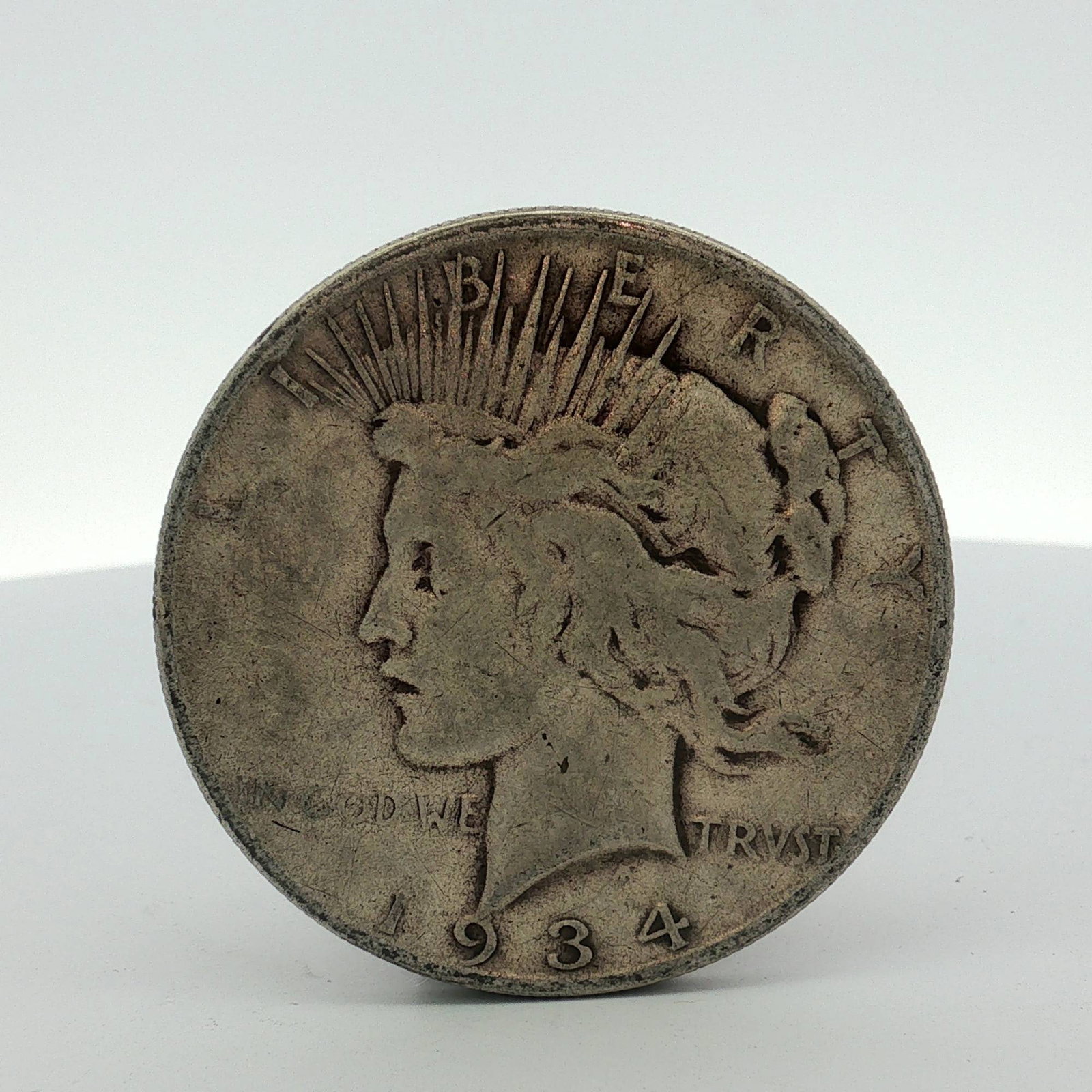 1934-S US Peace Silver Dollar: This US 1934-S Peace silver dollar is composed of 90% silver and 10% copper. The coin features the standard Peace dollar obverse and reverse designs. A visible S mint mark is located on the reverse to