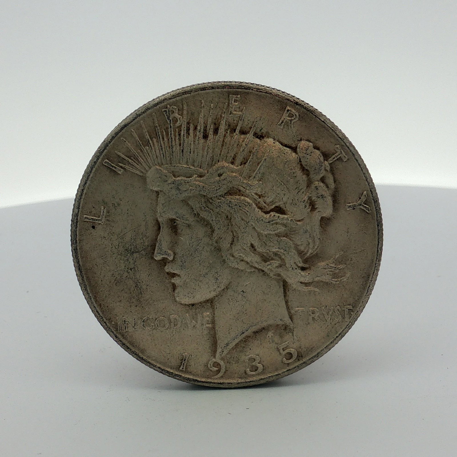 1935 US Peace Silver Dollar: This 1935 US Peace silver dollar is a one-dollar denomination coin. It features the Peace dollar obverse and reverse designs. Struck at the Philadelphia Mint, the coin lacks a mint mark on the