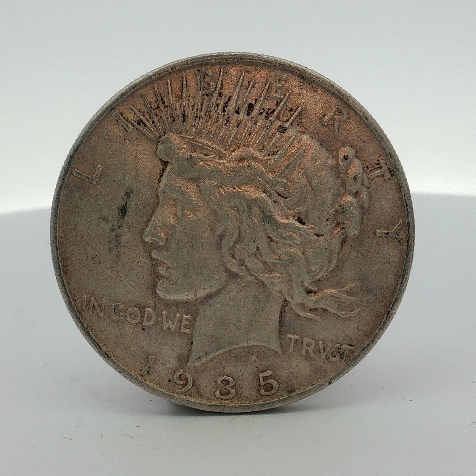 1935-S US Peace Silver Dollar: This US 1935-S Peace silver dollar is composed of 90% silver and 10% copper. The obverse features the Peace dollar Liberty head design with the inscriptions LIBERTY, IN GOD WE TRVST, and the date