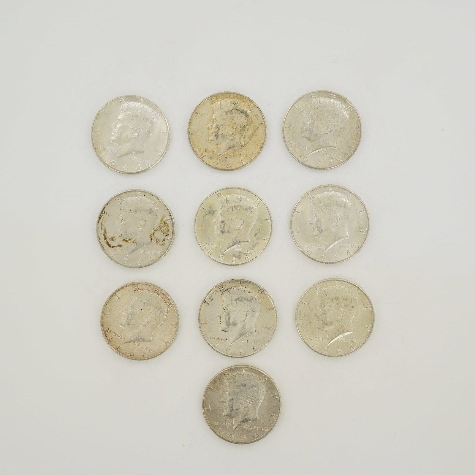 Ten 1964 US Kennedy Half Dollars $5.00 Face Value: A collection of ten US 1964 Kennedy half dollars with a total $5.00 face value. Each coin is struck in a composition of 90% silver and 10% copper. The obverse features the Kennedy profile and the reve