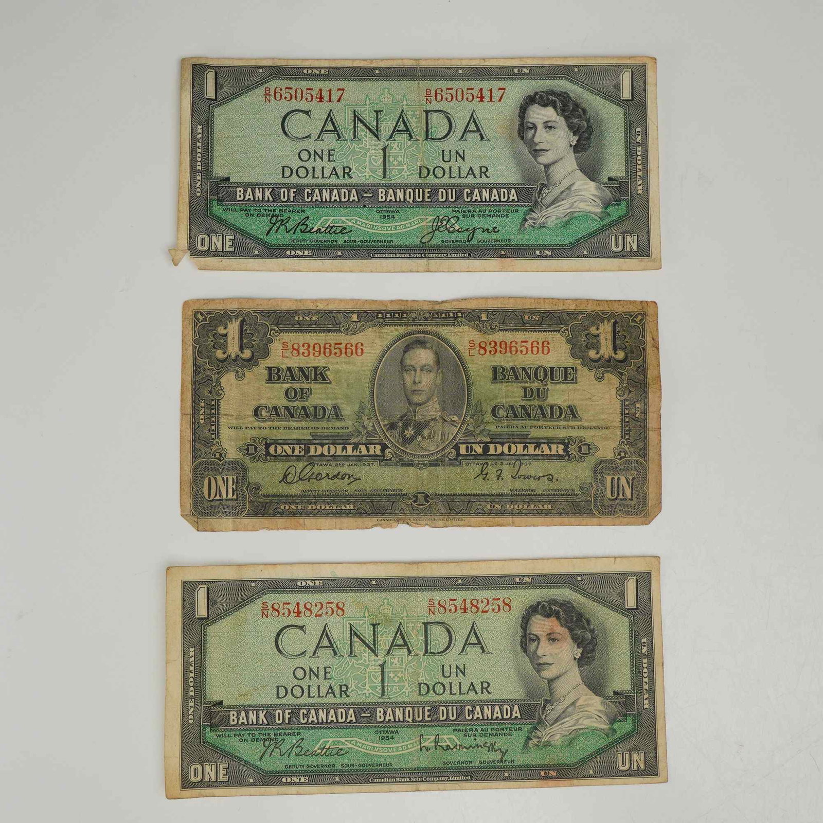 3pc 1937 and 1945 Canadian One-Dollar Banknotes: A collection of three Canadian one-dollar banknotes issued by the Bank of Canada (Banque du Canada). The group consists of one note from the 1937 series and two notes from the 1954 series. The 1937 se