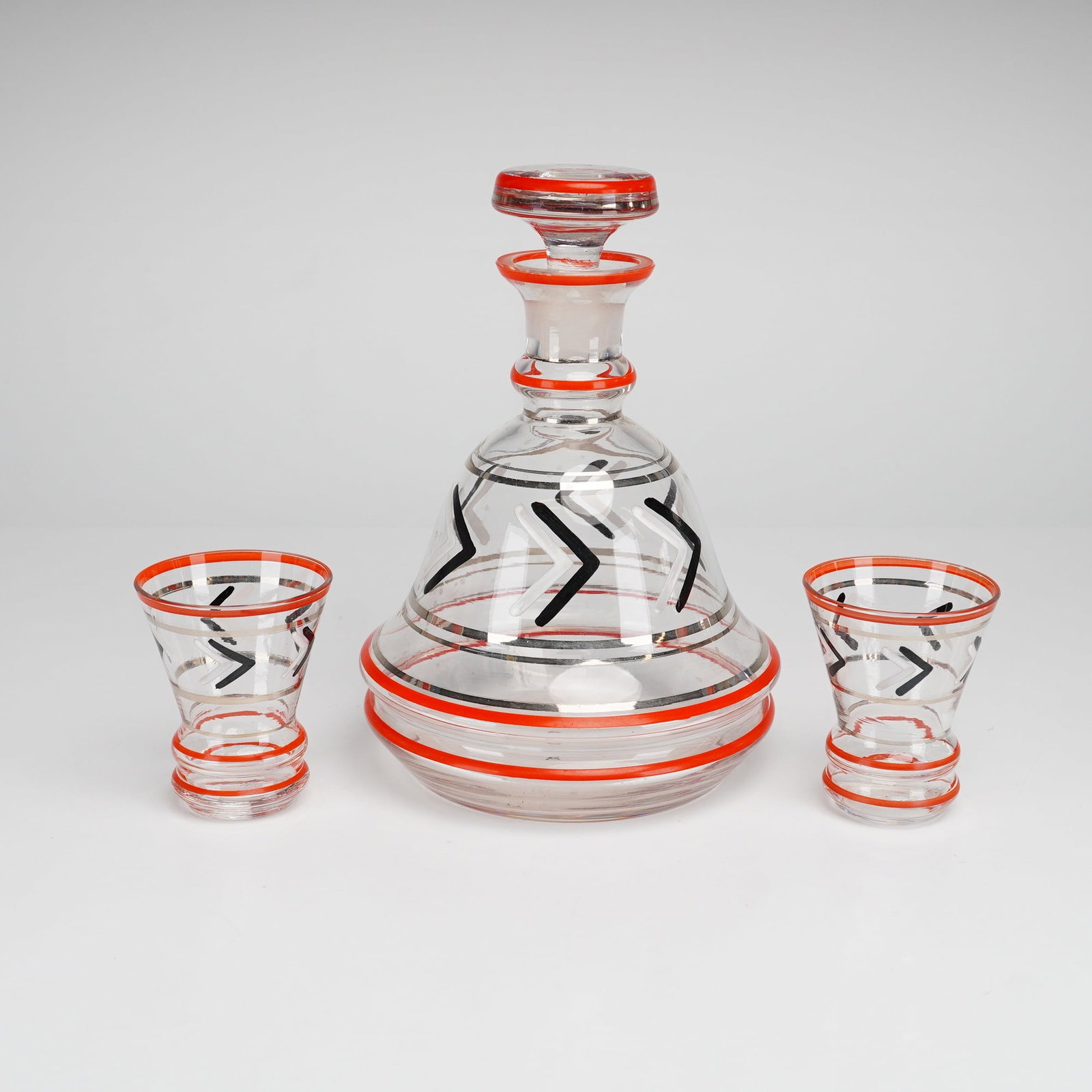 3pc Art Deco Enameled Glass Barware: A clear glass barware set from the Rubin Collection, comprising a decanter with a matching stopper and two coordinating glasses. The set is decorated with hand-enameled Art Deco geometric motifs, incl