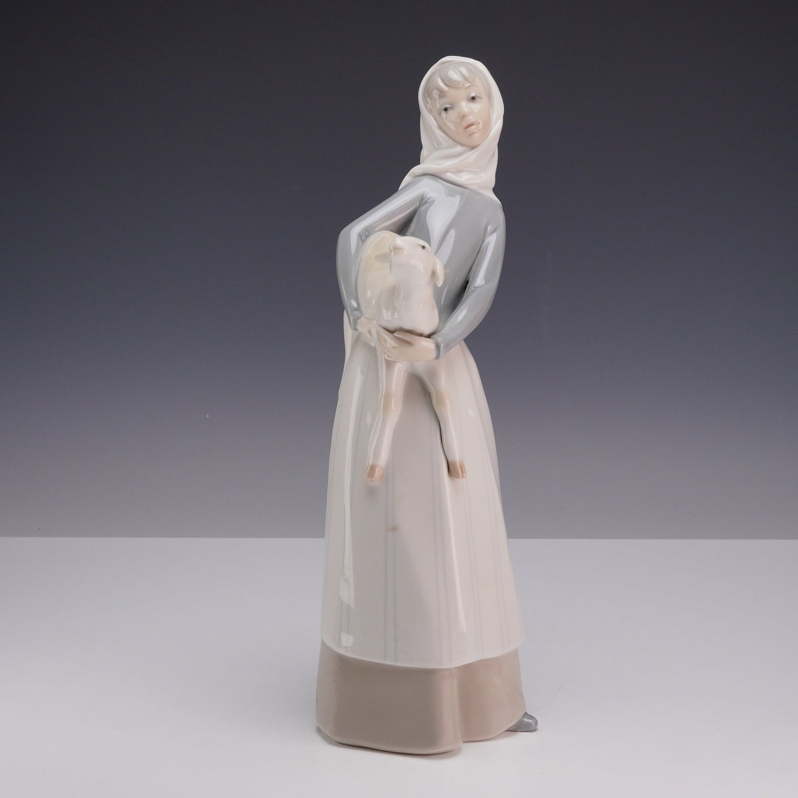 Lladro Porcelain Figurine Girl with Lamb Model 4584: A Lladro glazed porcelain figurine, model number 4585, depicting a young girl standing in a graceful pose, cradling a small lamb in her arms. She is dressed in traditional rustic attire, including a g