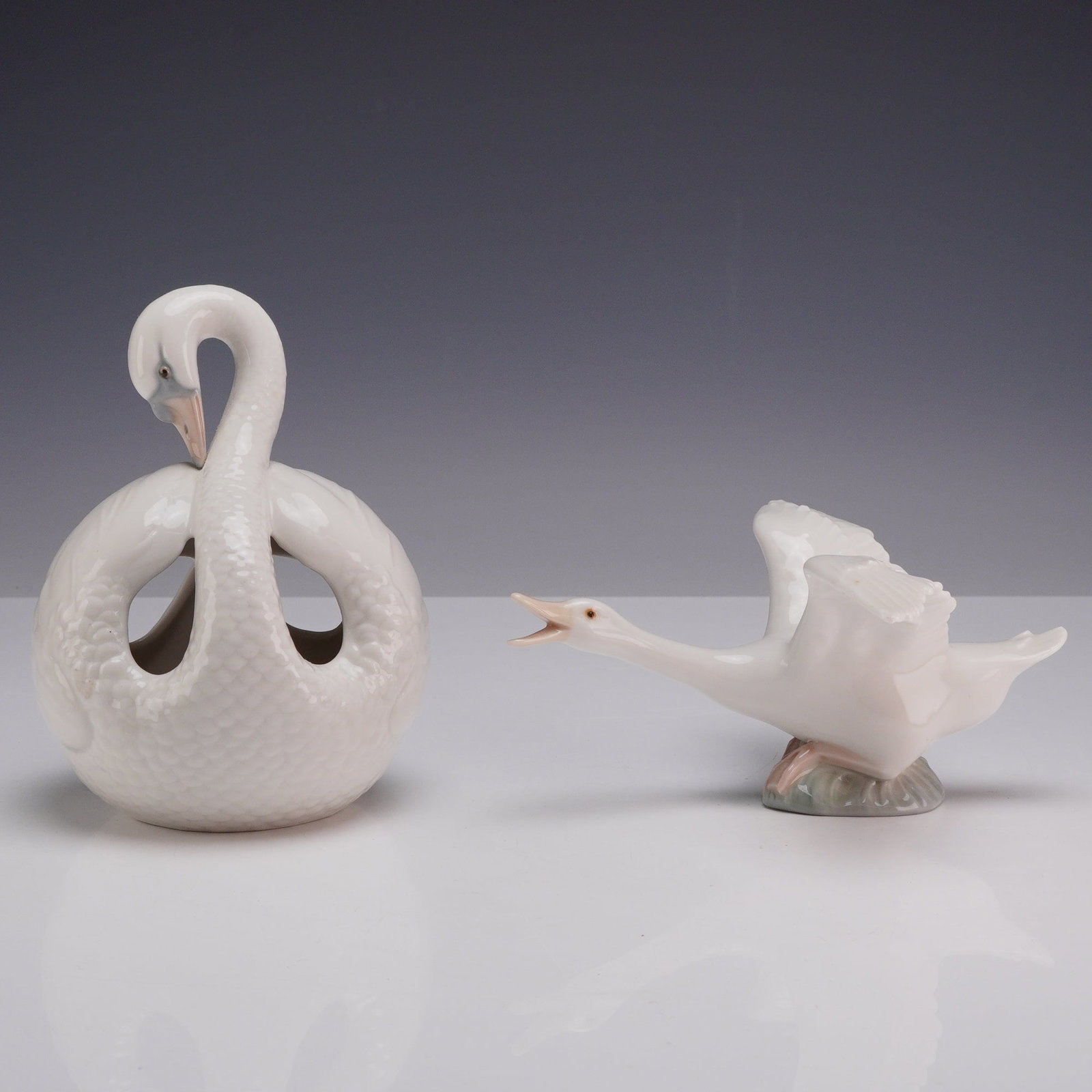 Two Lladro Porcelain Bird Figurines Including a Flying Duck: This lot features two glazed white porcelain figurines produced by the Lladro factory in Valencia, Spain. The first item is a flying duck figurine, depicted with outstretched wings and an extended nec