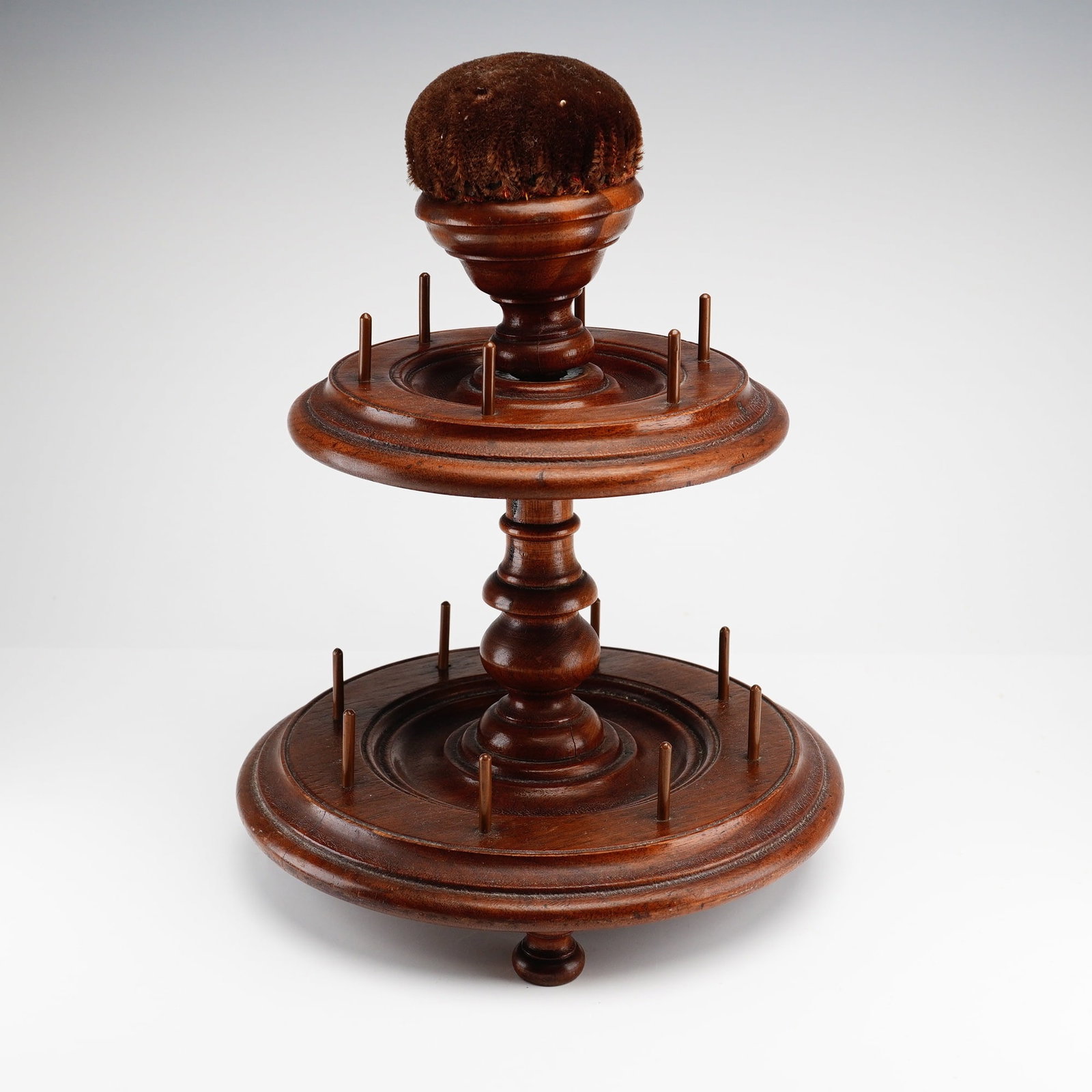 Victorian Two-Tier Turned Wood Bobbin and Spool Holder: This two-tiered wooden bobbin and spool holder is an antique sewing accessory designed as a thread carousel. It is constructed from a dark-stained hardwood and features a central turned pedestal